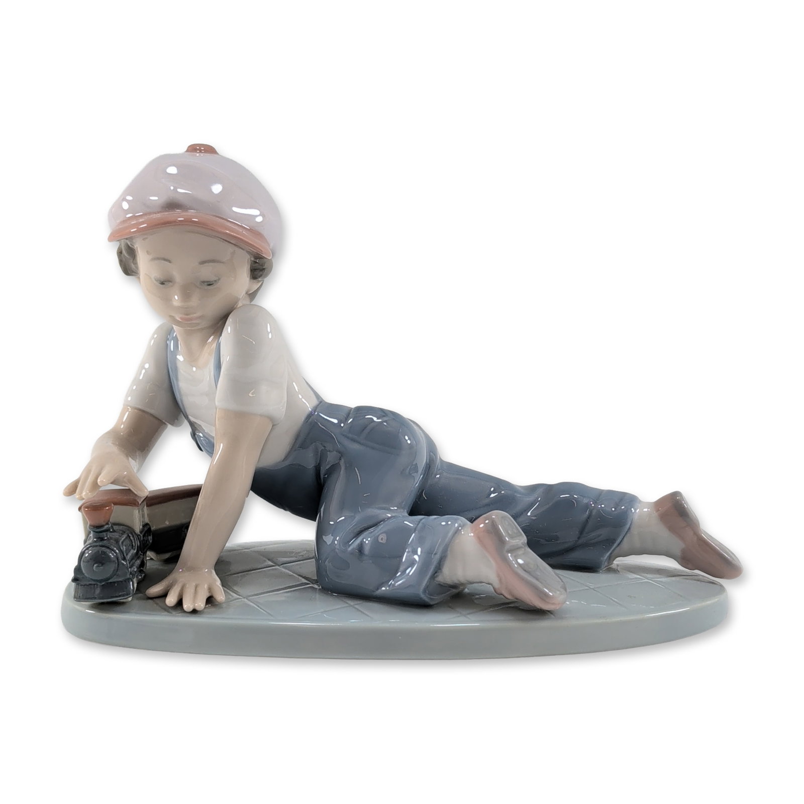 Lladro Spanish Porcelain Figurine All Aboard: Lladro (Spain) glazed porcelain figurine titled All Aboard, model number 7619. The piece depicts a young boy in blue overalls, a white t-shirt, and a lavender cap, positioned on a grey circular base w