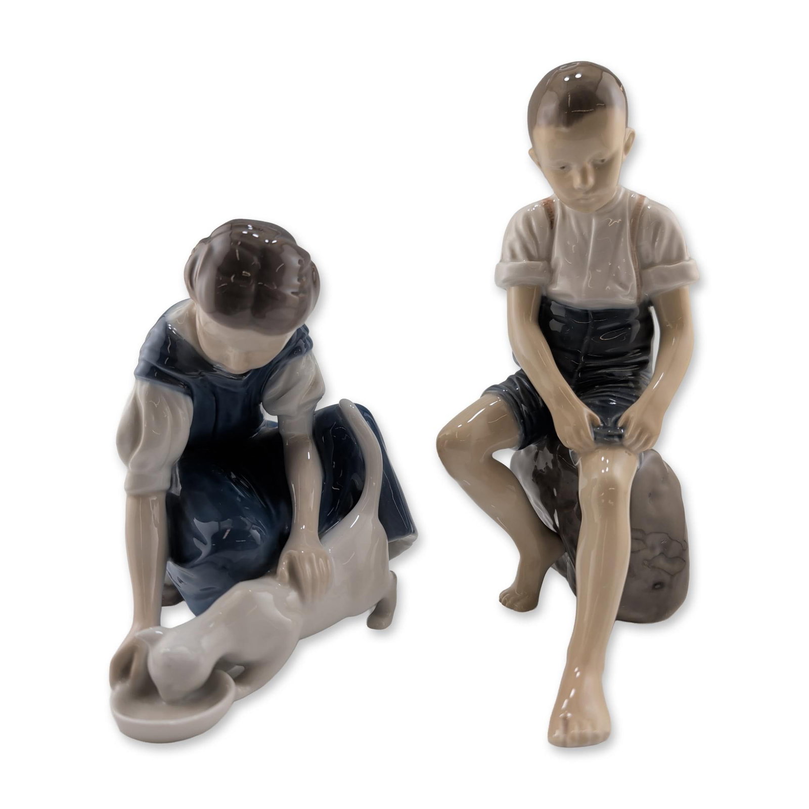 Two Bing and Grondahl Porcelain Figurines: Pair of Danish glazed porcelain figurines produced by Bing and Grondahl. The collection includes a figurine of a seated boy, model number 1757, and a figurine of a kneeling girl feeding a cat, model n