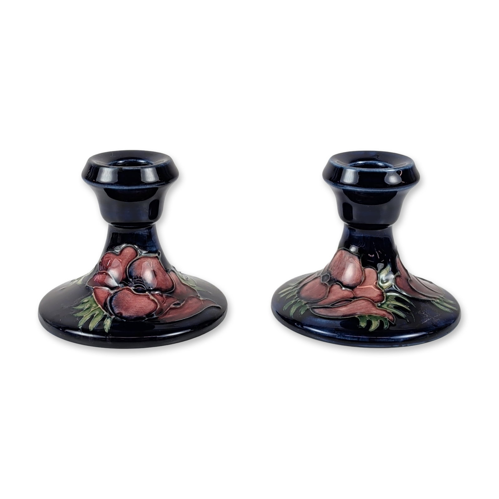 Pair of Moorcroft Anemone Pottery Candlesticks: Moorcroft (English) pair of flared-base dwarf candlesticks in glazed earthenware, featuring the Anemone pattern. The floral decoration is hand-painted in shades of red, pink, and purple with green