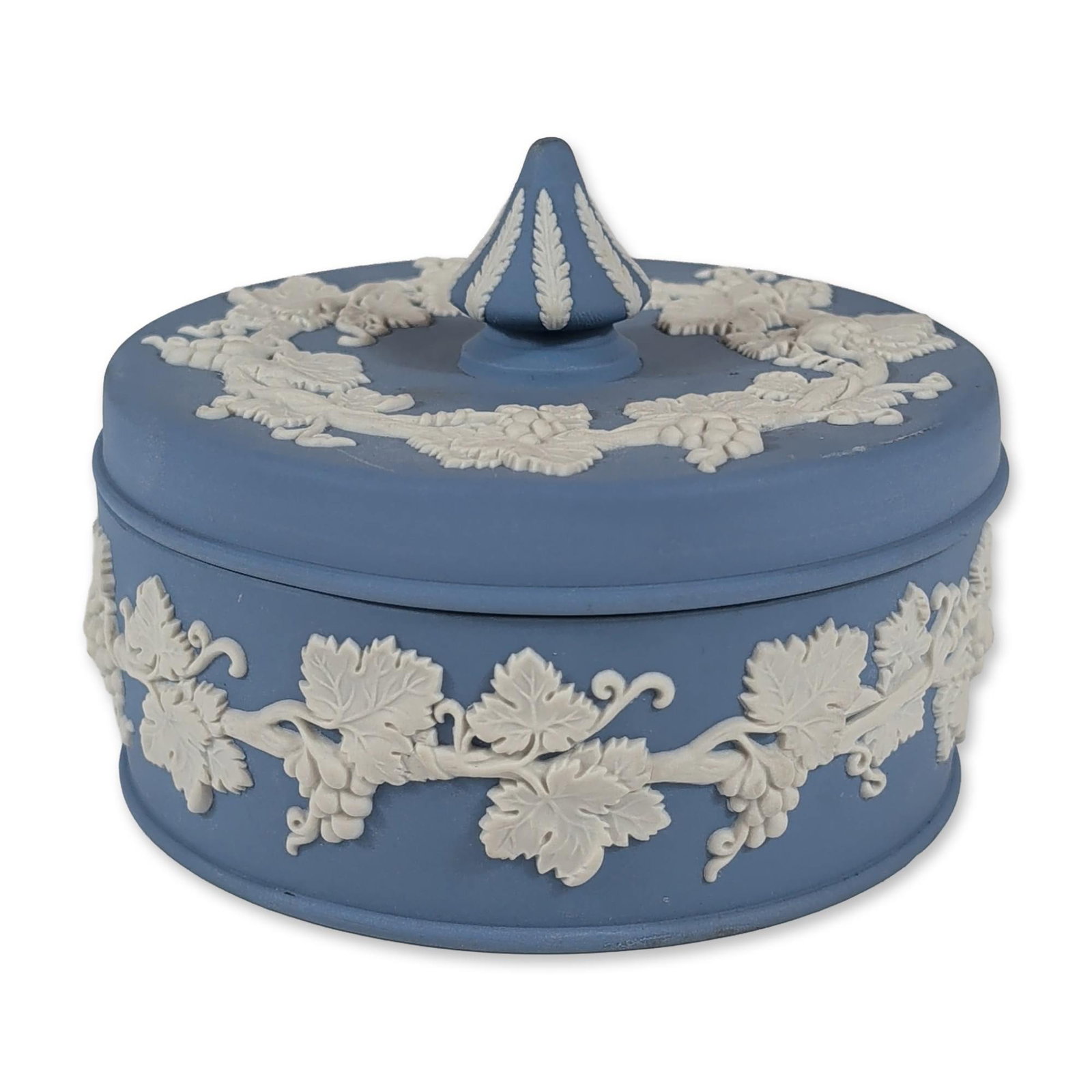 Wedgwood Blue Jasperware Grapevine Lidded Box: Wedgwood pale blue jasperware circular lidded box featuring white bas-relief grapevine decoration. The lid is detailed with a central foliate-ribbed finial and a surrounding grapevine wreath. The body