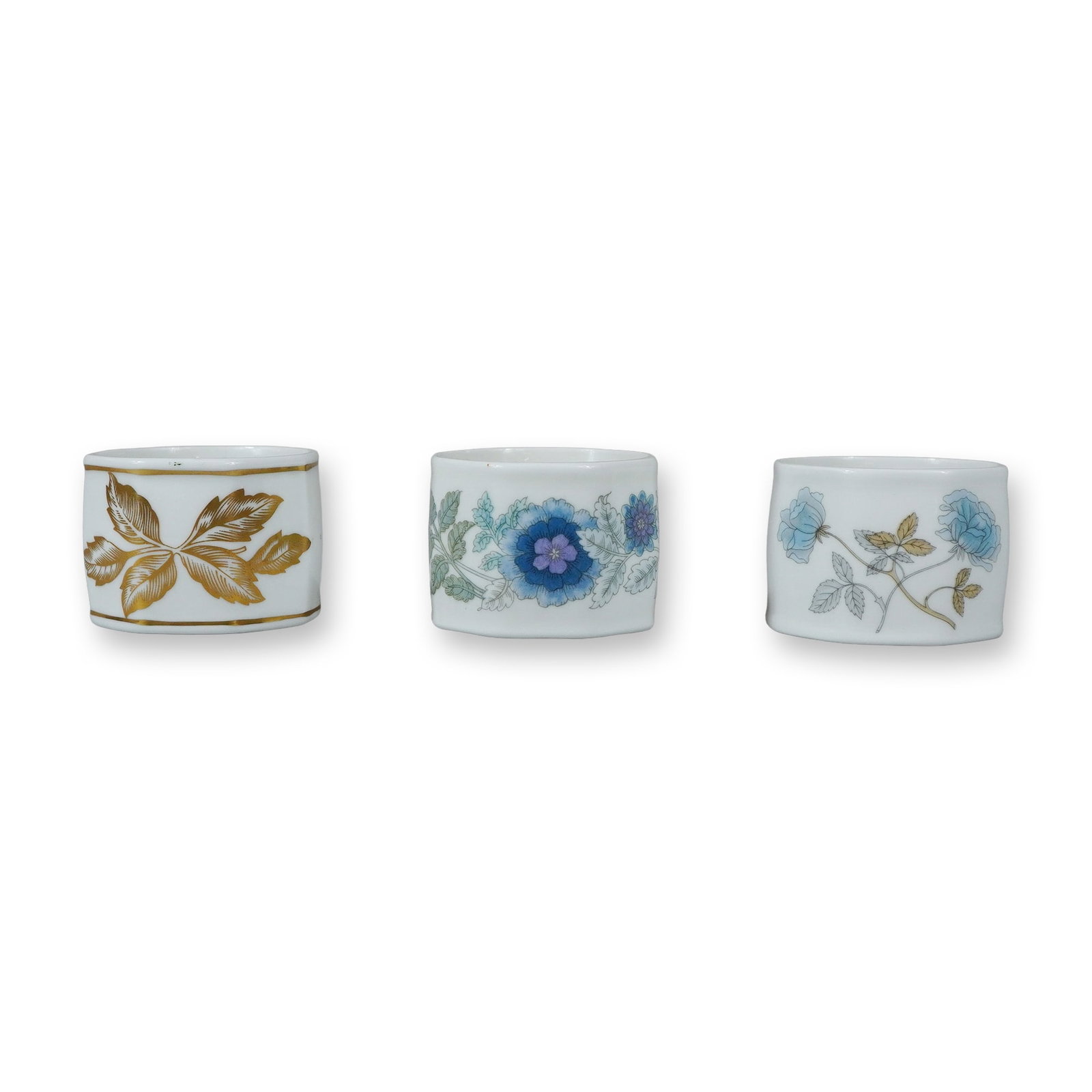 3pc Wedgwood Bone China Napkin Rings: A trio of English bone china napkin rings produced by Wedgwood. Each ring features a faceted octagonal exterior and a smooth cylindrical interior. The group includes three distinct patterns. One ring 
