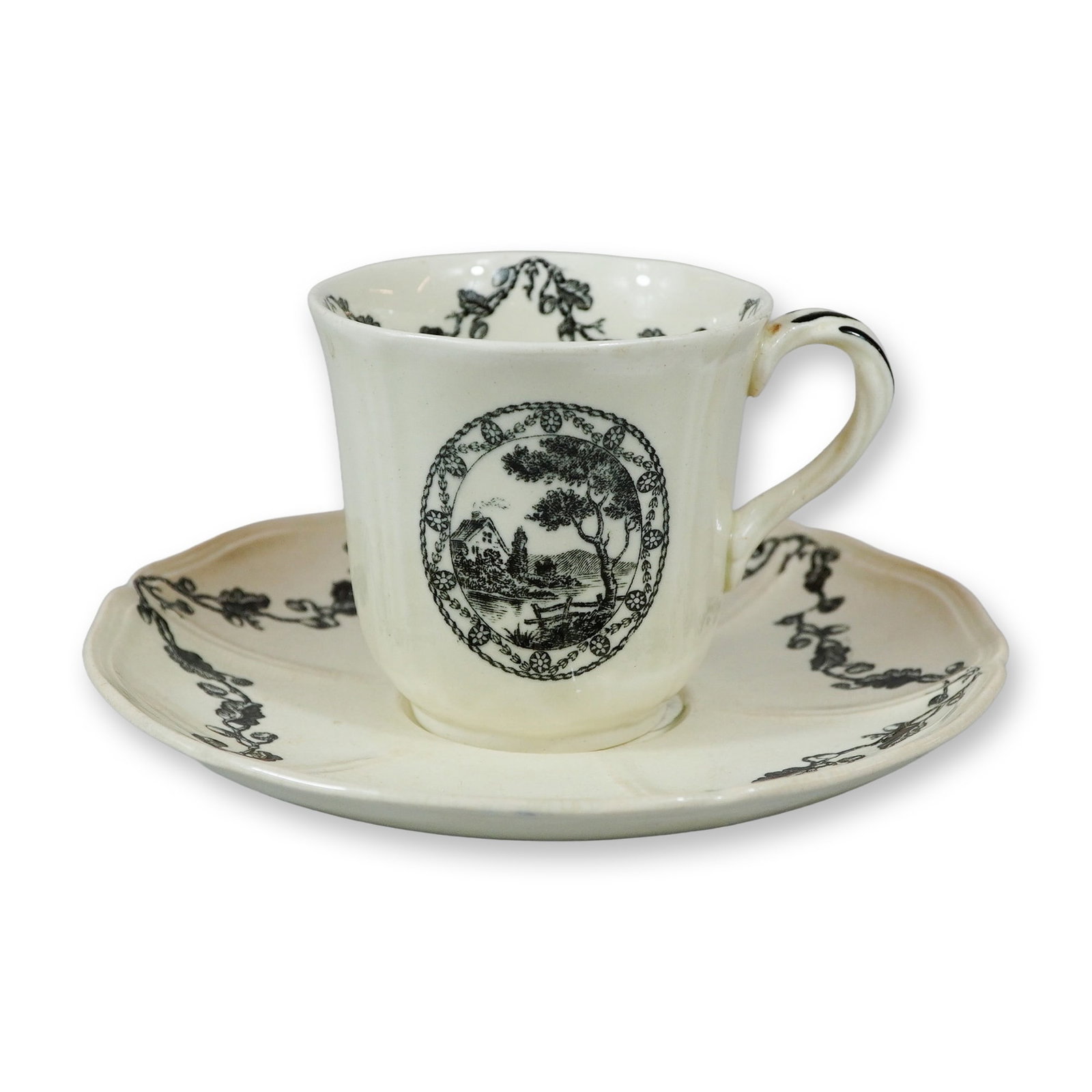 2pc Wedgwood Bewick Black Transferware Cup and Saucer: A Wedgwood cream-colored earthenware cup and saucer in the Bewick pattern featuring black transfer-printed decoration. The exterior of the cup displays a circular landscape vignette in a woodcut style