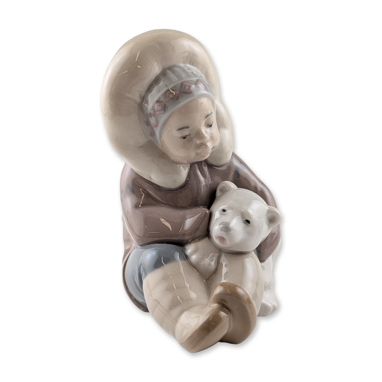 Lladro 1195 Eskimo Porcelain Figurine: Lladro (Spain). Glazed porcelain figurine titled Eskimo, reference number 1195. Sculpted by Juan Huerta, the piece depicts a seated child in a traditional hooded parka cradling a polar bear cub. The f