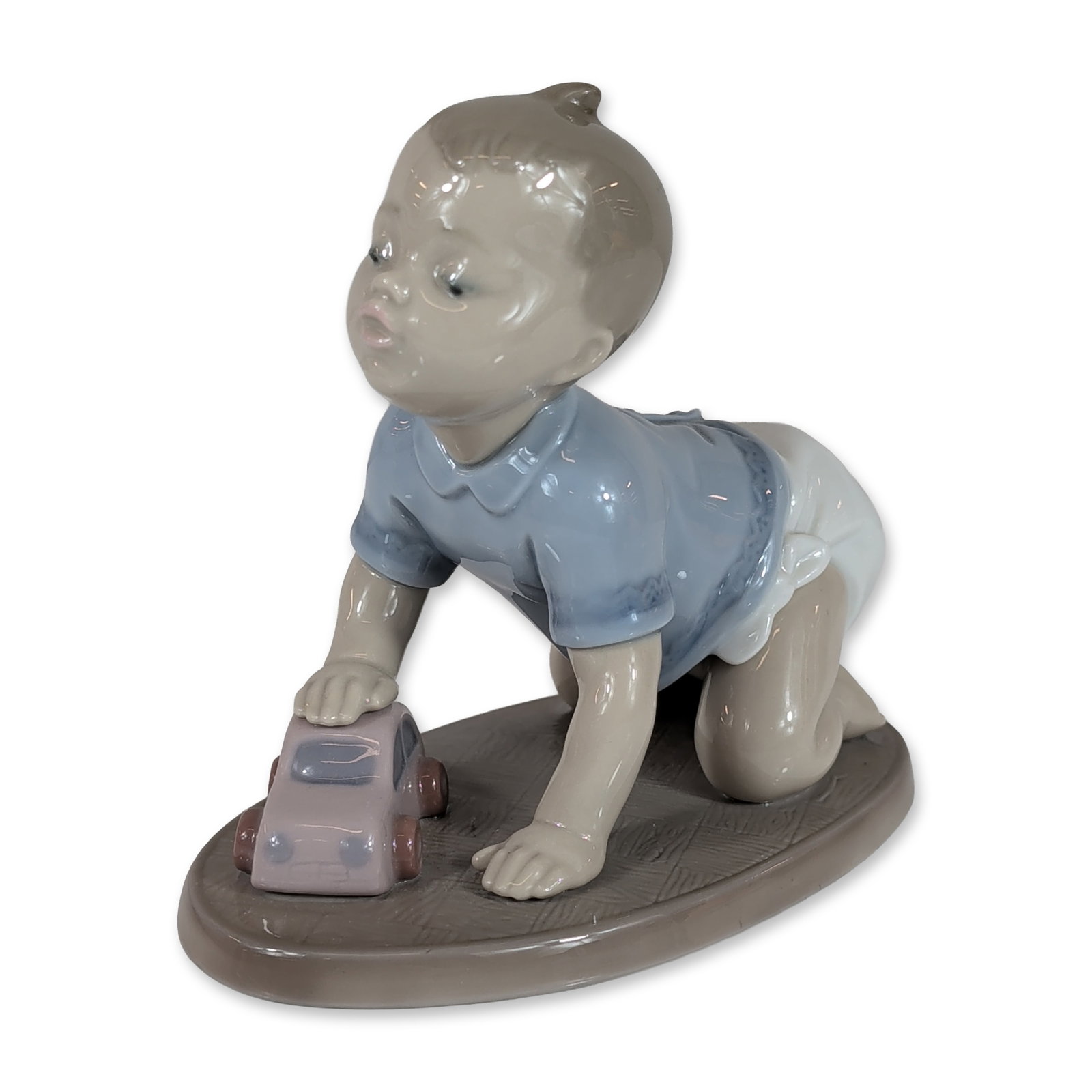 Lladro Spanish Porcelain Ready to Roll Figurine 01006429: Lladro, Spain. Glazed porcelain figurine titled Babys First Car (Cochecito de Juguete), model number 6429. The piece depicts a crawling infant wearing a pale blue collared shirt and white diaper on a 
