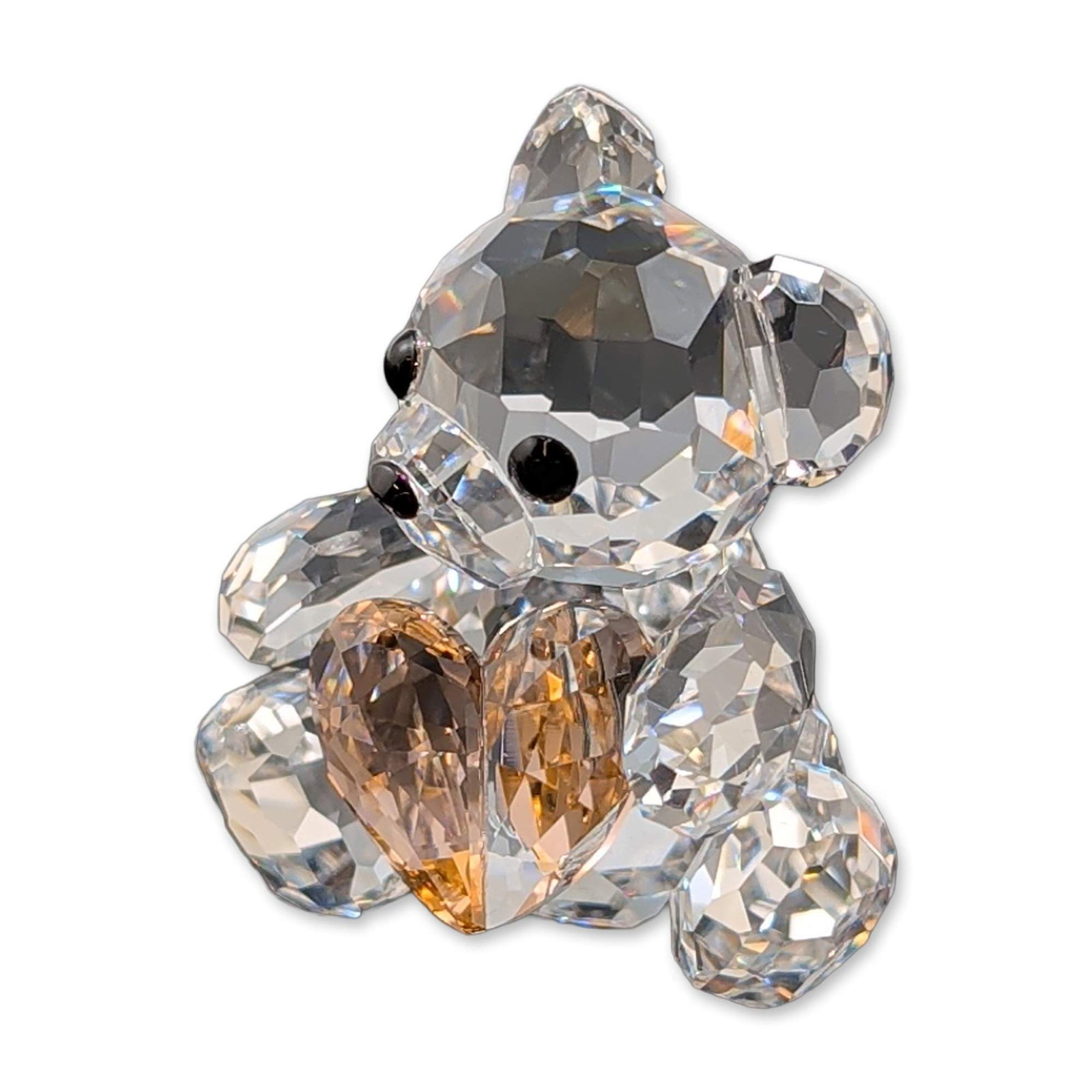 Swarovski Crystal Kris Bear Figurine, From the Heart: Swarovski Kris Bear figurine in faceted lead glass crystal, depicting a seated bear holding a faceted heart in a half honey half clear tone. The bear features small black crystal accents for the eyes 