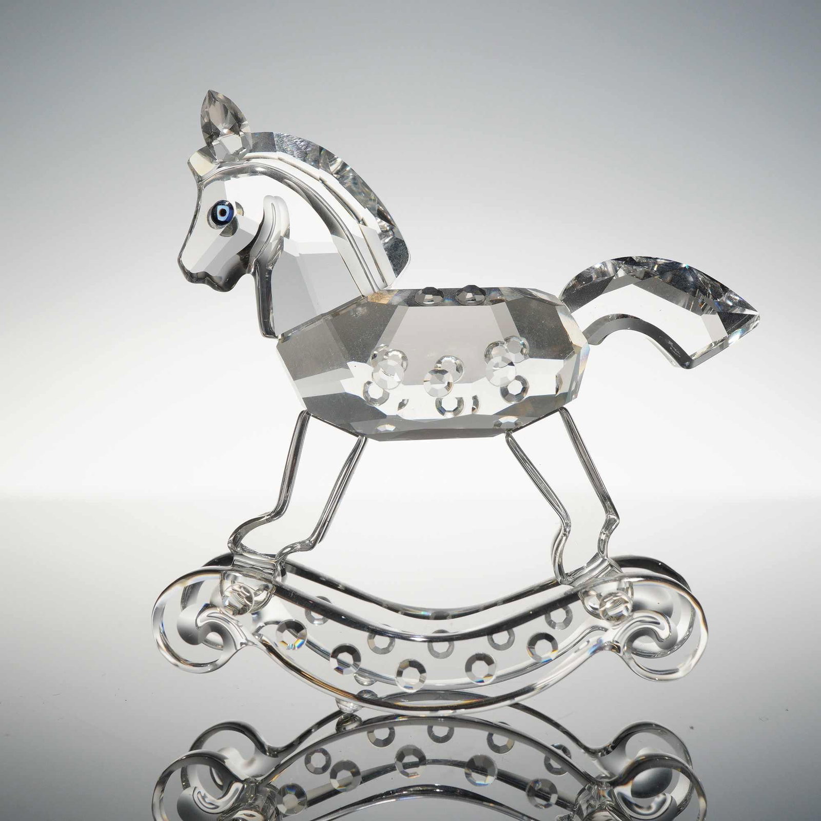Swarovski Crystal Rocking Horse Figurine: Swarovski Silver Crystal rocking horse figurine, featuring a faceted clear crystal body detailed with circular indentations along the sides, a smooth-sculpted head and neck with a faceted mane, blue c