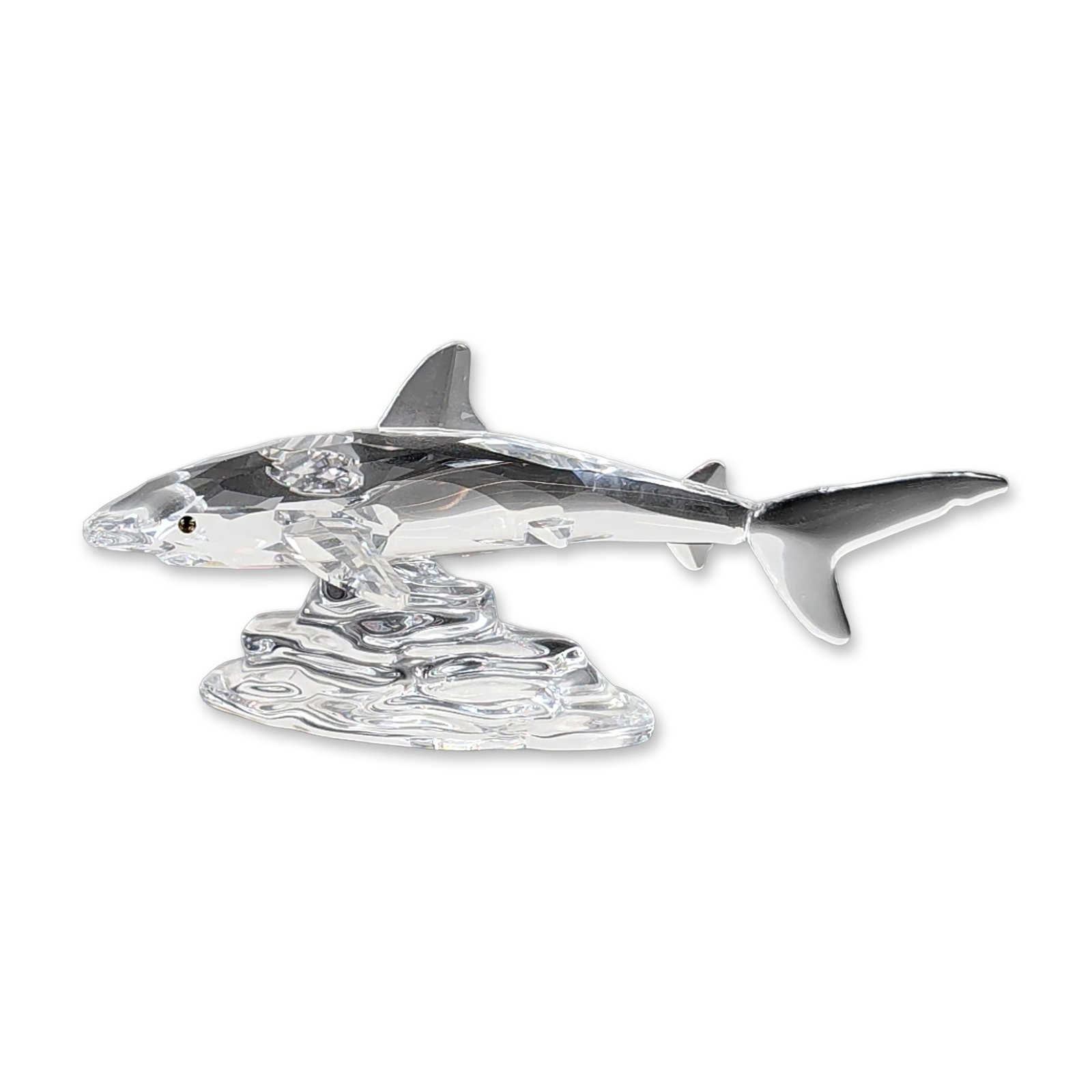 Swarovski Crystal Shark and Wave Figurine: This Swarovski crystal figurine showcases a faceted shark riding a smooth crystal wave. The shark features inset multicolored eyes and sharply defined dorsal and pectoral fins. The wave base has a rip