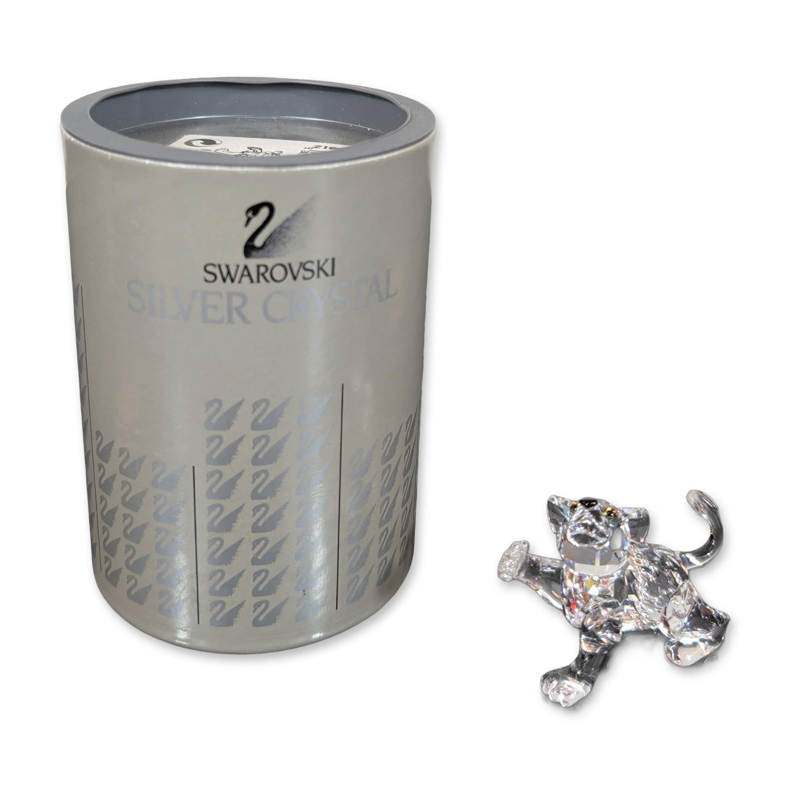 Swarovski Silver Crystal Lion Cub: Crystal Lion Cub figurine in faceted clear lead crystal, featuring colored eyes and a black stone nose. Etched Swarovski swan logo and copyright symbol on the underside of a rear paw. Includes origina