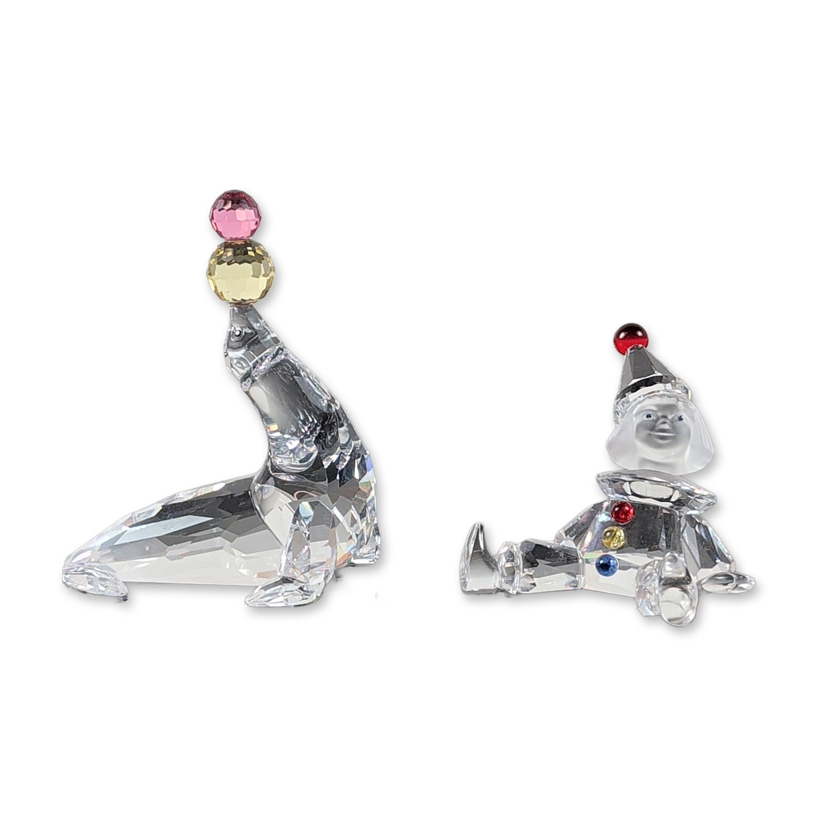 2pc Swarovski Faceted Crystal Figurines Collection: A Swarovski collection showcasing faceted crystal figurines includes a puppet figurine, model 217207, adorned with vibrant red, yellow, and blue crystal accents and topped with a jester hat, as well a