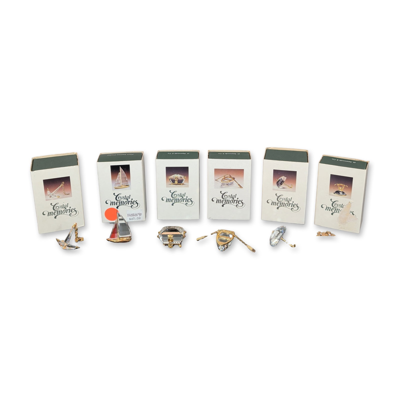 6pc Swarovski Crystal Memories Figurines: Swarovski collection of six miniature figurines in faceted lead crystal and gold-tone metal, including an Island, umbrella, anchor, treasure chest, sailboat, and boat with oars. Packaging marked for C