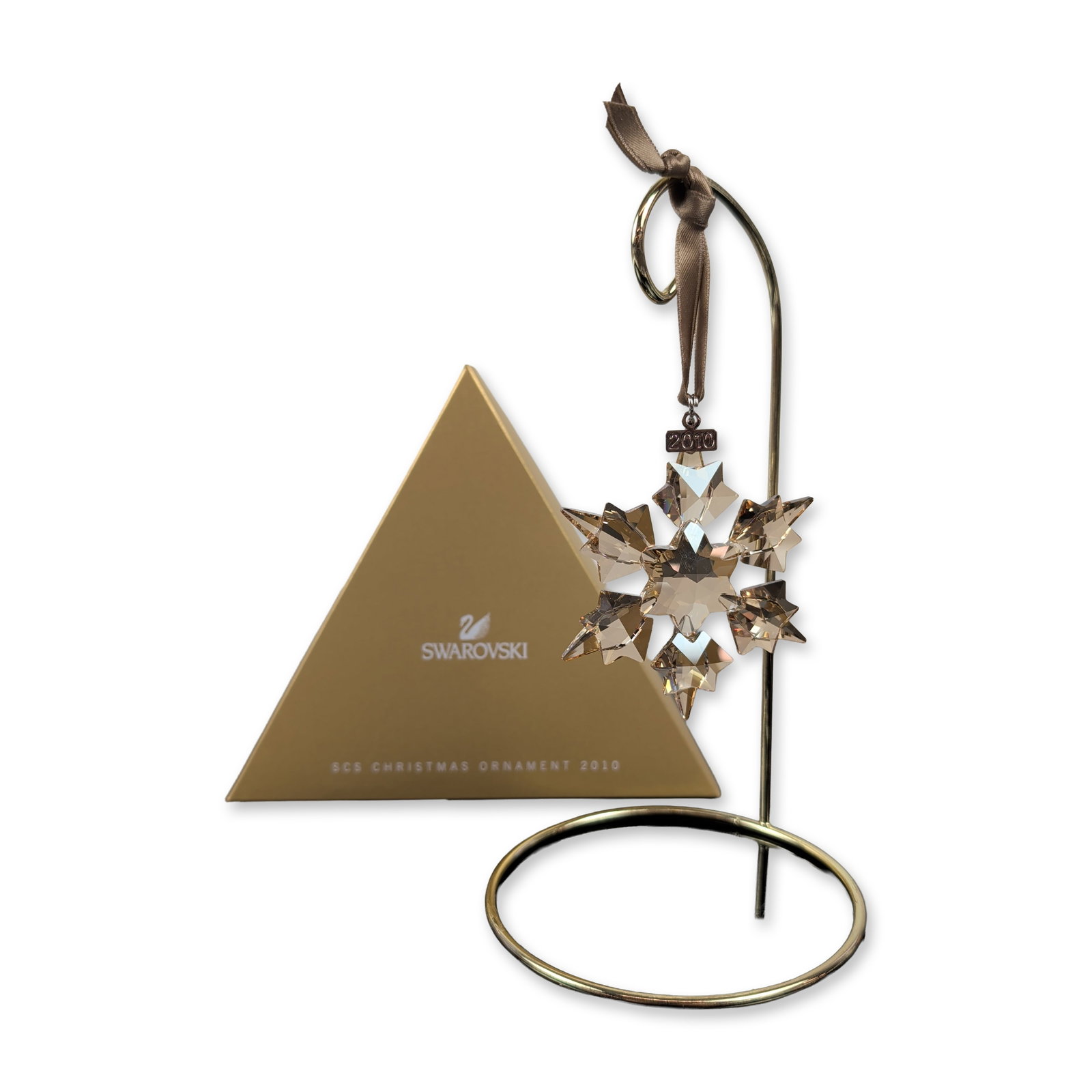 Swarovski SCS 2010 Gold Tone Crystal Ornament: Swarovski Crystal Society Annual Edition Christmas ornament in faceted Golden Shadow crystal. Features a six-pointed star form suspended by a brown satin ribbon with gold-toned metal hardware. Include