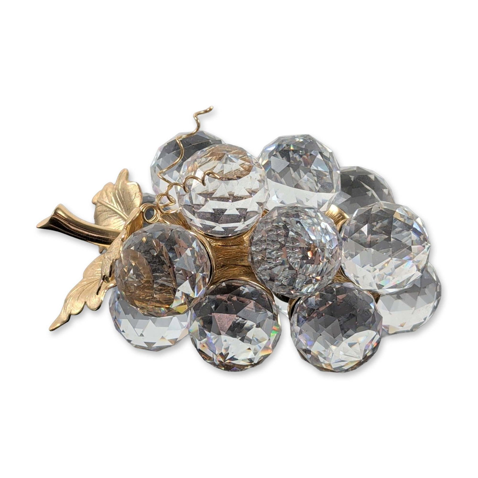 Swarovski Crystal Grape Cluster Brooch: Swarovski crystal grape cluster brooch featuring fifteen faceted clear lead crystal spheres. The gold-toned metal setting is designed with two textured leaves, a vertical stem, and curled wire tendril
