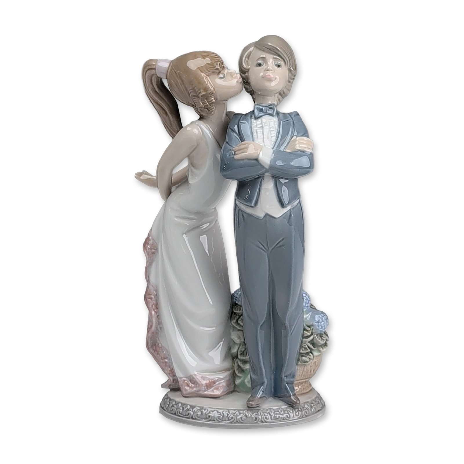 Lladro Glazed Porcelain Figurine, Lets Make Up 01005555: Glazed porcelain figurine titled Lets Make Up designed by Juan Huerta. The scene depicts a young boy in a blue tuxedo with crossed arms standing next to a young girl in a white evening gown with pink 