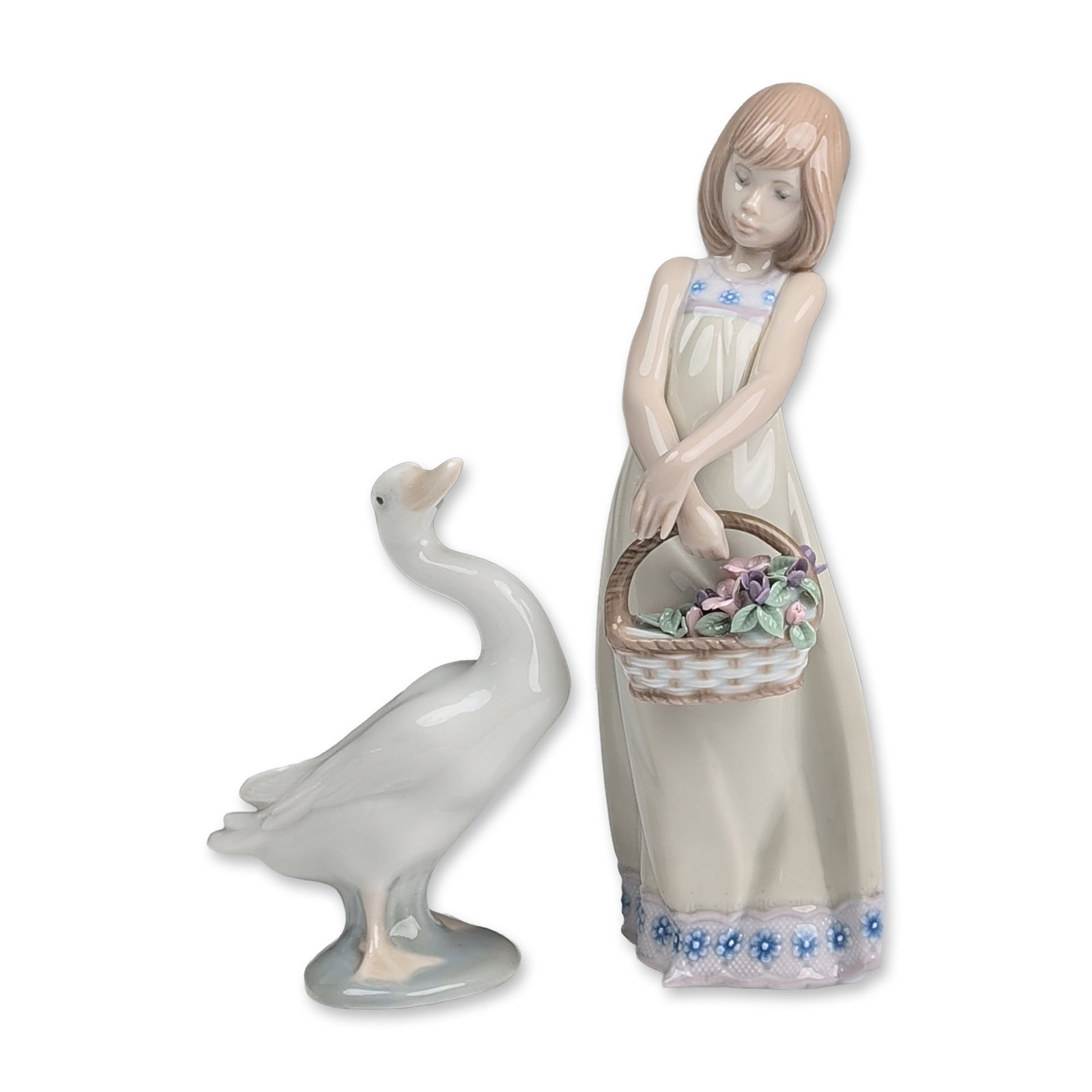 2pc Lladro Porcelain Figurines, Floral Treasures & Little Duck: Two glazed porcelain figurines, including a young girl and a goose. The taller figure depicts a girl in a long pale grey dress with blue floral motifs, carrying a woven-textured basket filled with ind