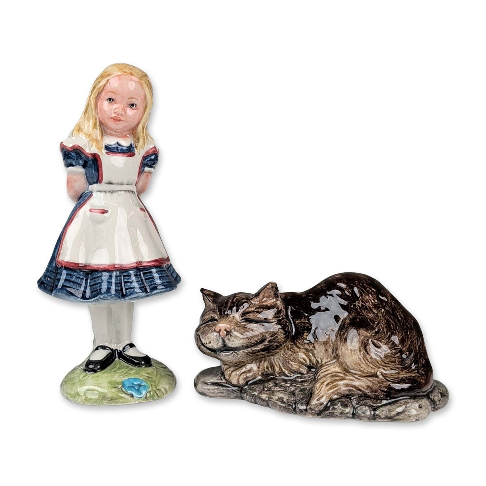 Pair of Beswick Alice Series Figurines: Beswick, England. Pair of figurines in glazed ceramic from the Alice Series. The grouping includes Alice, depicted in a blue dress with a white pinafore, and the Cheshire Cat, modeled as a brown-toned