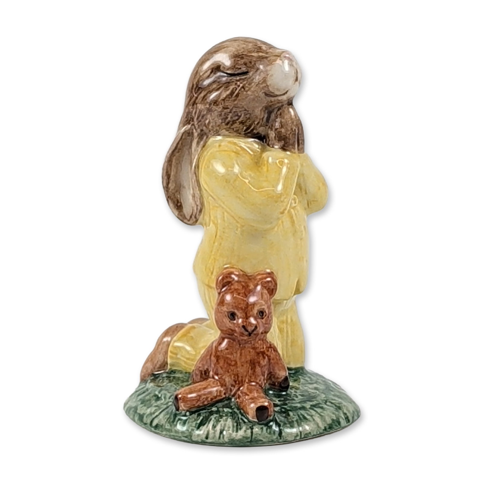 Royal Doulton Bedtime Bunnykins Porcelain Figurine DB 103: Royal Doulton. Figurine in glazed porcelain, titled Bedtime Bunnykins, model DB 103. The piece depicts a rabbit in yellow pajamas kneeling in prayer upon a textured green base, accompanied by a small 