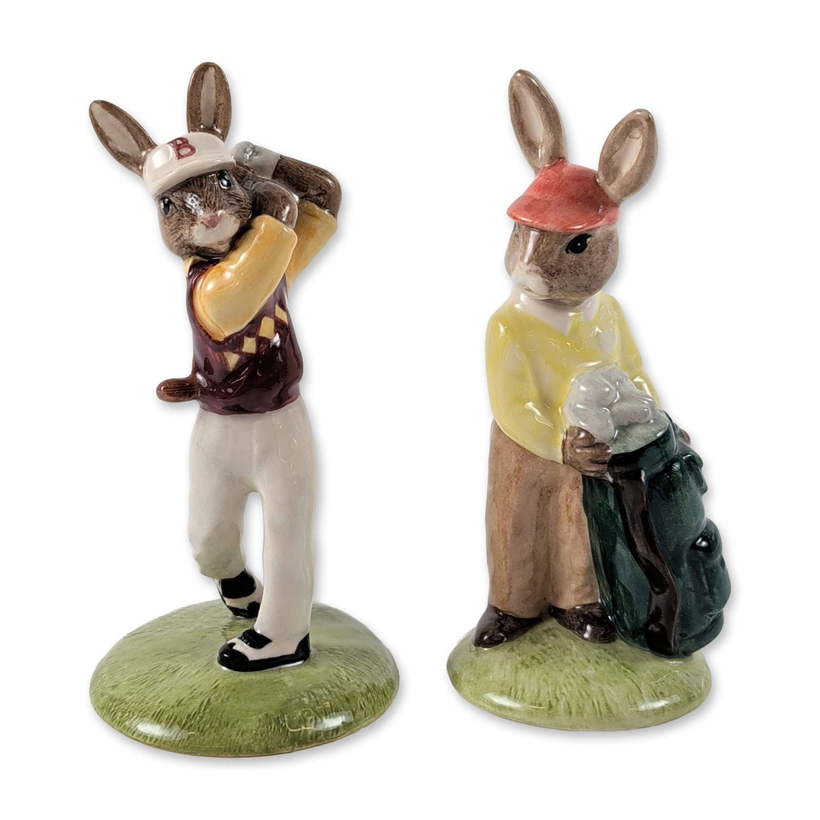 2pc Royal Doulton Bunnykins Golfing Figurines: Royal Doulton. Pair of figurines in hand-decorated porcelain from the Bunnykins series, including the Caddie (DB 271) and Golfer (DB 255). The Caddie is modeled wearing a red cap and yellow sweater wh