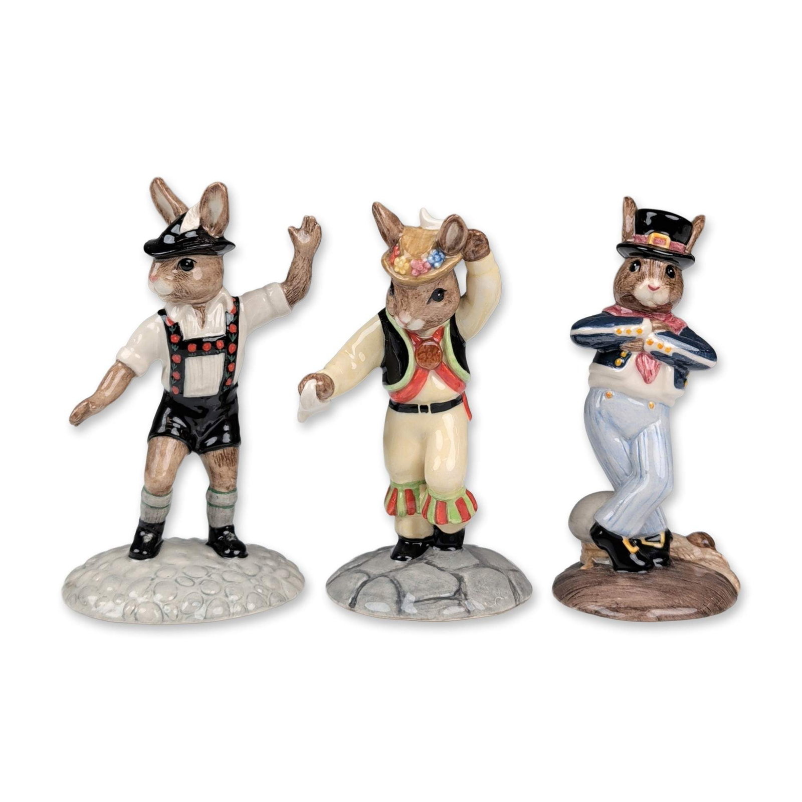 Royal Doulton Bunnykins Dancer Figurine Trio: Royal Doulton. Three hand-decorated porcelain Bunnykins figurines featuring traditional dance themes. The collection includes Tyrolean Dancer (DB 242) in Alpine dress with lederhosen and floral suspen