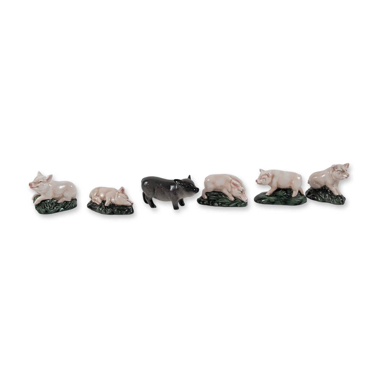 Collection of Six Royal Doulton Porcelain Pig Figurines: Collection of six glazed porcelain pig figurines produced by Royal Doulton. The group features five pink-toned pigs on green mound bases and one solid black pig. Models include one black walking pig (