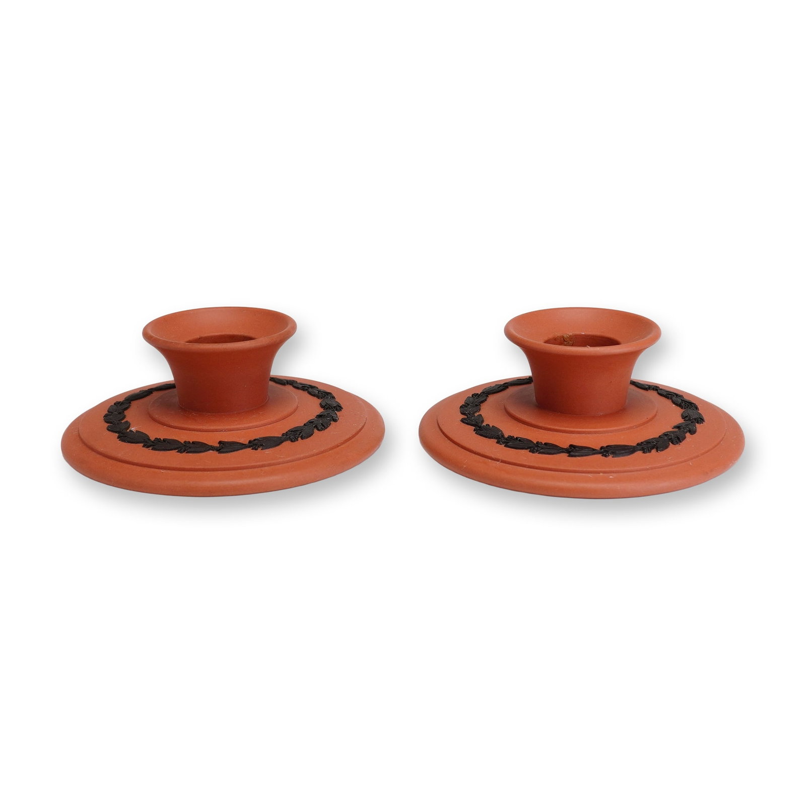 2pc Wedgwood Jasperware Rosso Antico and Black Basalt Candle Holders: This is a pair of Wedgwood Jasperware candle holders crafted in Rosso Antico red stoneware with black basalt sprigged decoration. Each piece features a low, circular disc form with a central flared ca