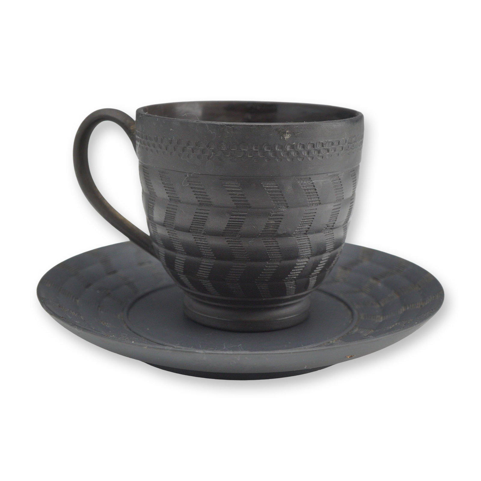 Wedgwood Black Basalt Cup and Saucer: A Wedgwood black basalt tea cup and matching saucer crafted from fine-grained unglazed stoneware. Both pieces feature intricate engine-turned decoration consisting of a rhythmic chevron or basketweave