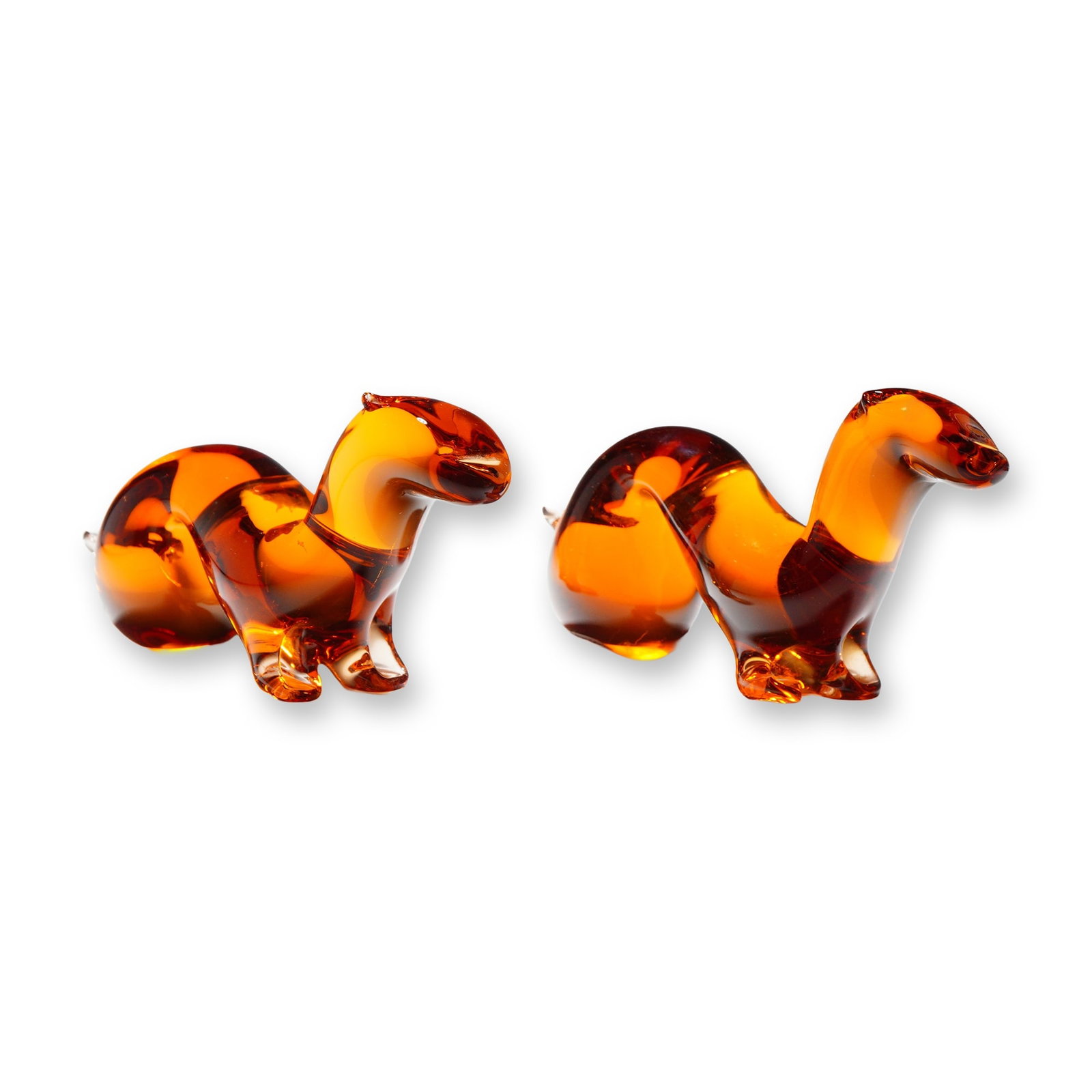 A Pair of Wedgwood Amber Glass Stoat Figurines: A pair of stylized art glass figurines depicting stoats, produced by Wedgwood in England. Each piece is crafted from solid-blown, translucent amber-colored glass, featuring a minimalist, fluid, arched