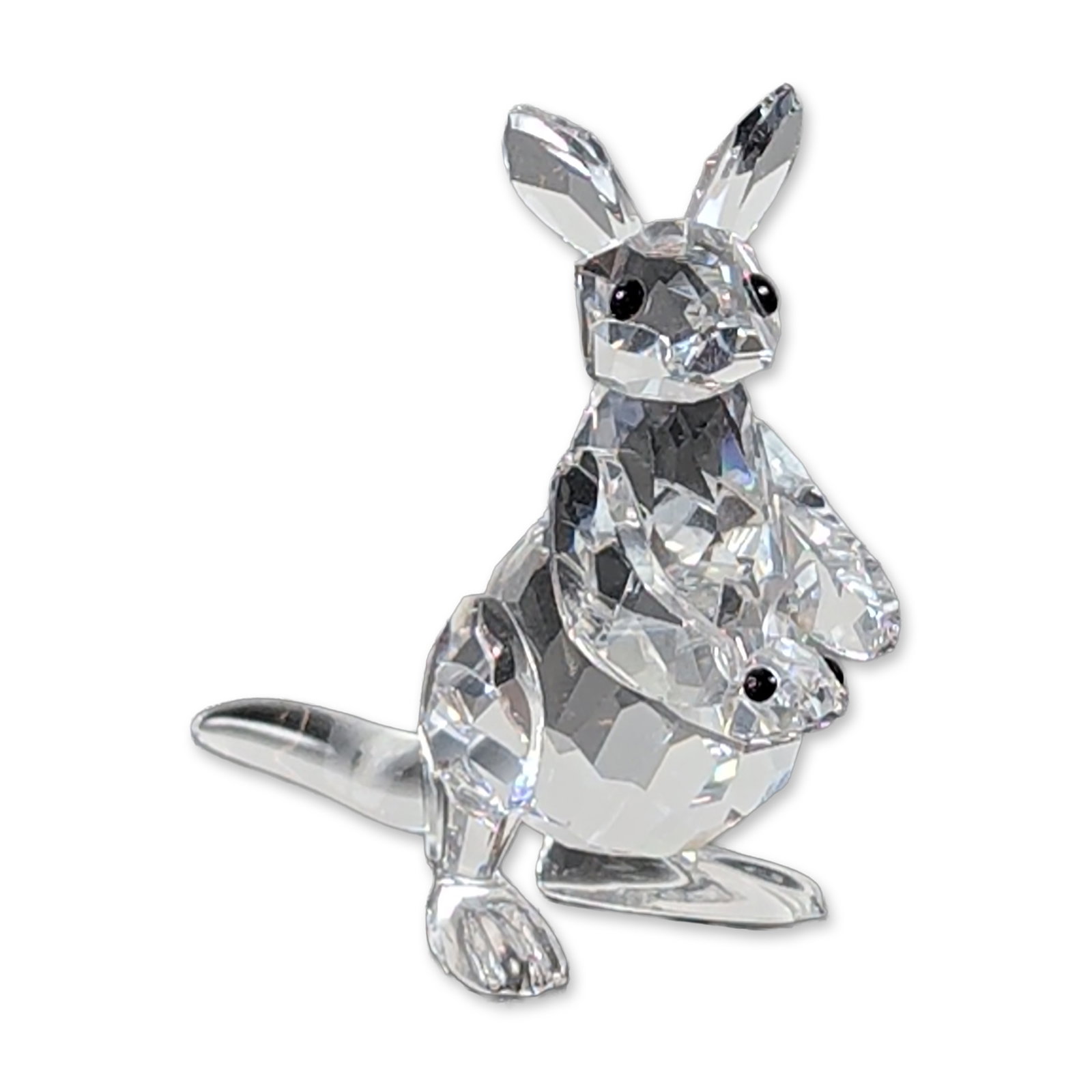 Swarovski Crystal Kangaroo with Joey Figurine: Swarovski. Kangaroo with joey figurine in clear lead crystal, featuring a multi-faceted body and head contrasted by smooth, polished ears and tail. The mother kangaroo is depicted with two black cryst