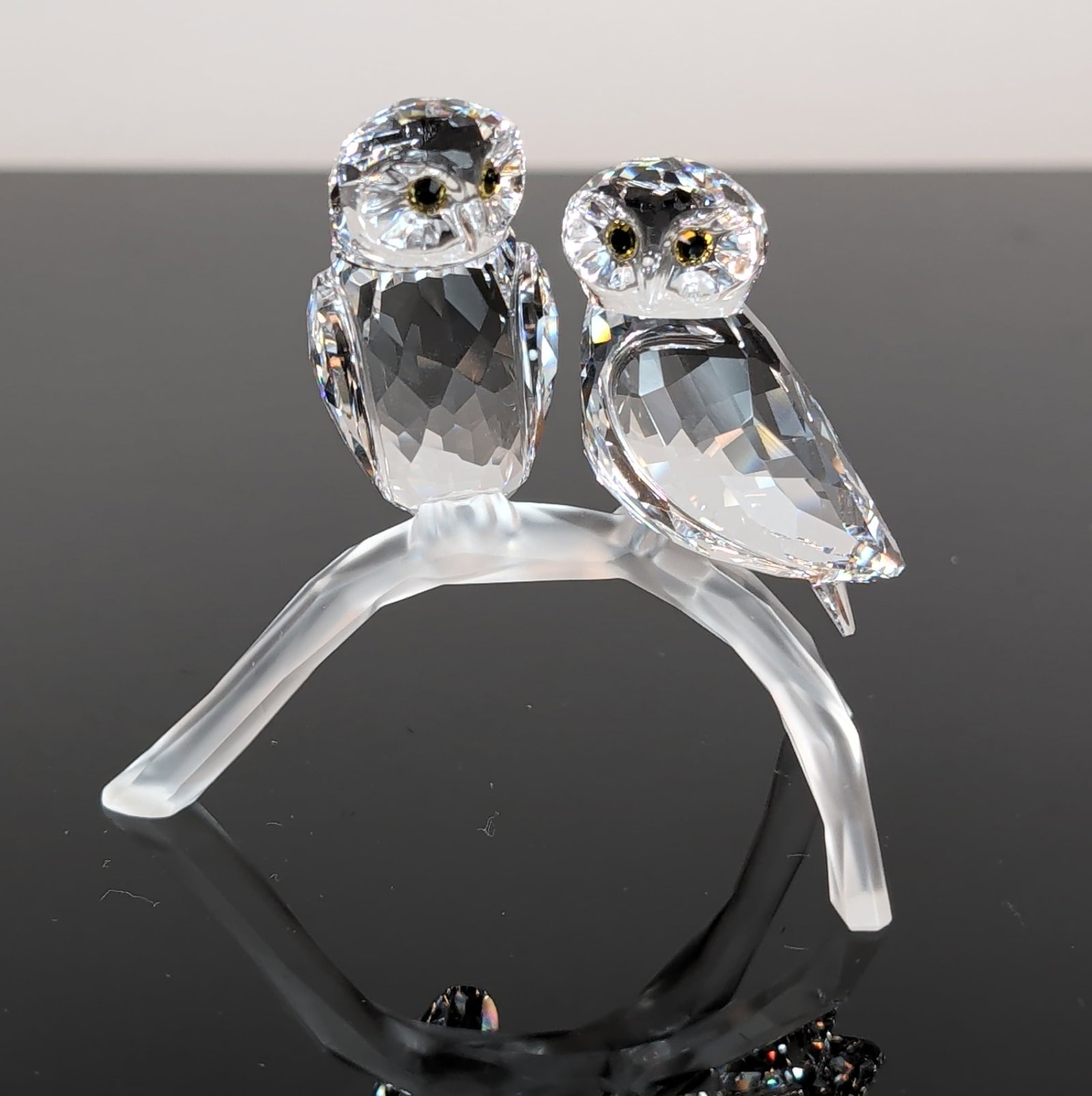 Swarovski Crystal Owls on Branch: Swarovski crystal figurine titled Owls, featuring two faceted clear crystal owls perched on a frosted glass branch. Each owl is accented with dark-colored faceted crystal eyes with amber centers. The 