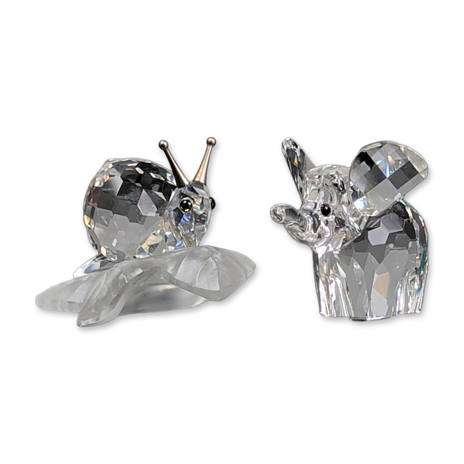 2pc Swarovski Crystal Figurines, Snail on Leaf and Small Elephant: Swarovski Silver Crystal group of two figurines, including a small elephant and a snail on a leaf. The small elephant features a faceted crystal body, with ears and trunk raised and black bead eyes. T