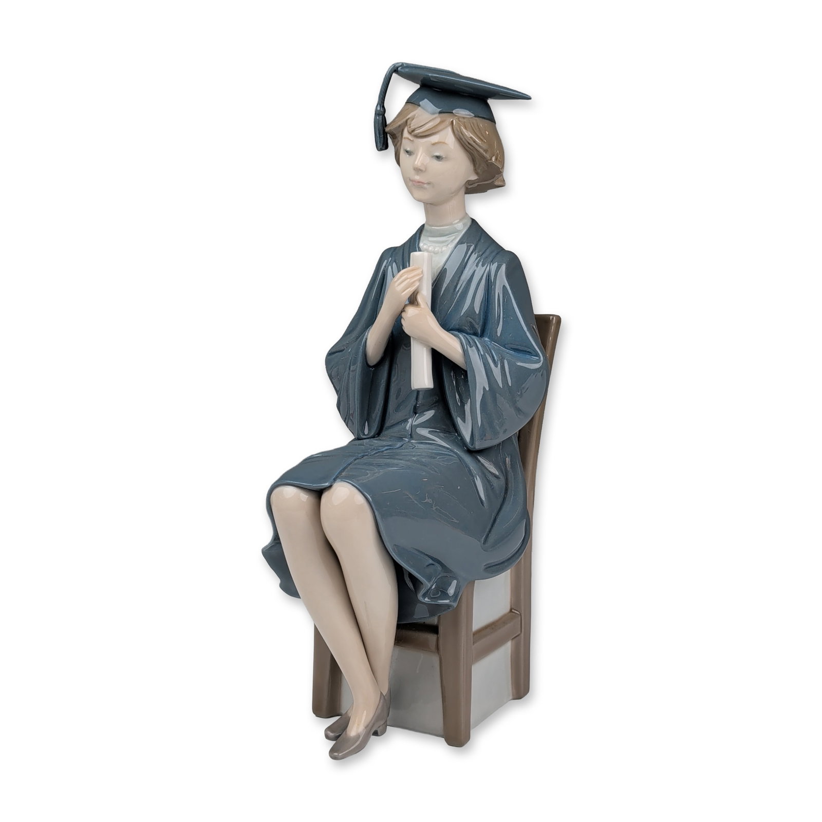 Lladro Glazed Porcelain Figurine, Girl Graduate 01005199: Figurine in glazed porcelain, model number 5199, designed by Francisco Catala. The figure depicts a seated young woman in a blue academic gown and mortarboard holding a diploma. Underside features the