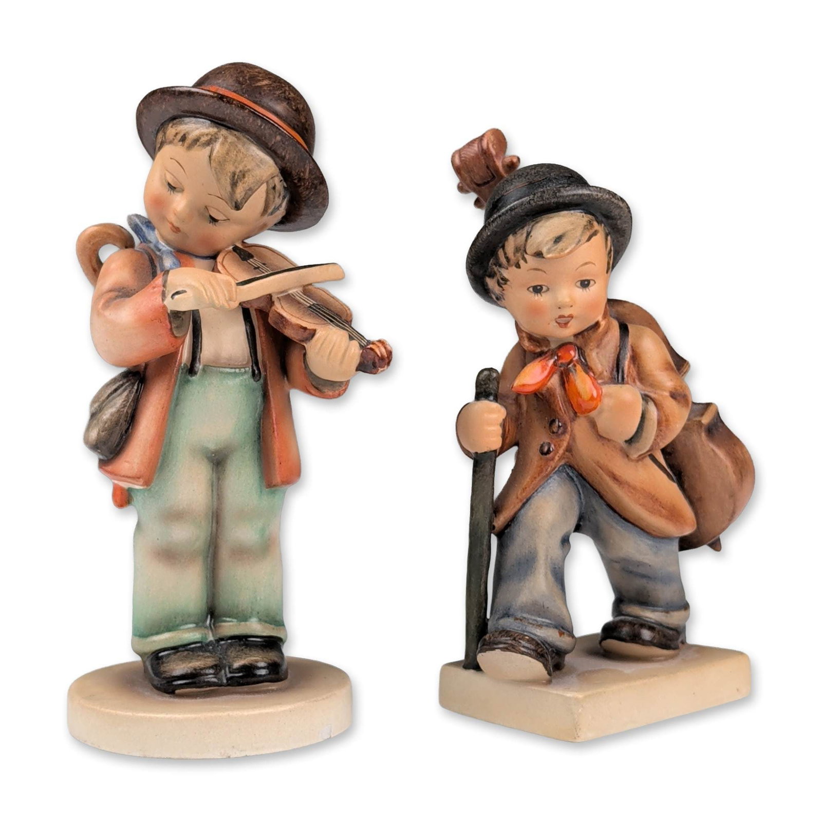 2pc Goebel Hummel Porcelain Figurines, Little Fiddler and Little Cellist: Goebel Hummel. Pair of hand-painted ceramic figurines with matte glazes. Includes the Soloist model featuring a traveling boy musician with a double bass and walking stick on a rectangular base, and t