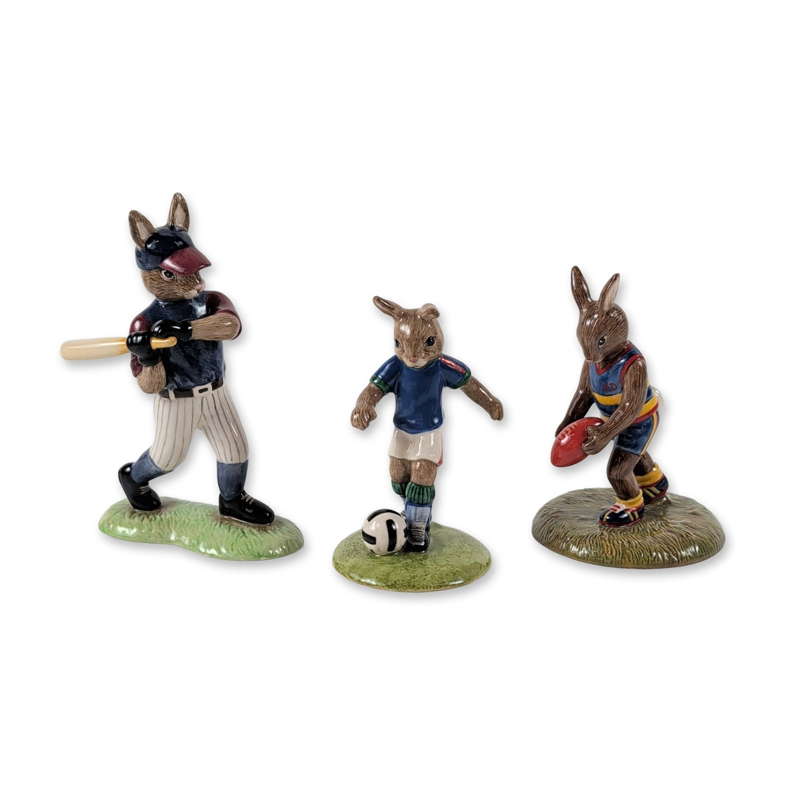 3pc Royal Doulton Bunnykins Sports Figurines: Trio of Royal Doulton Bunnykins hand-decorated earthenware figurines, each depicting a rabbit participating in a different sport. The set comprises Aussie Rules Bunnykins (DB 508), Soccer Bunnykins (D