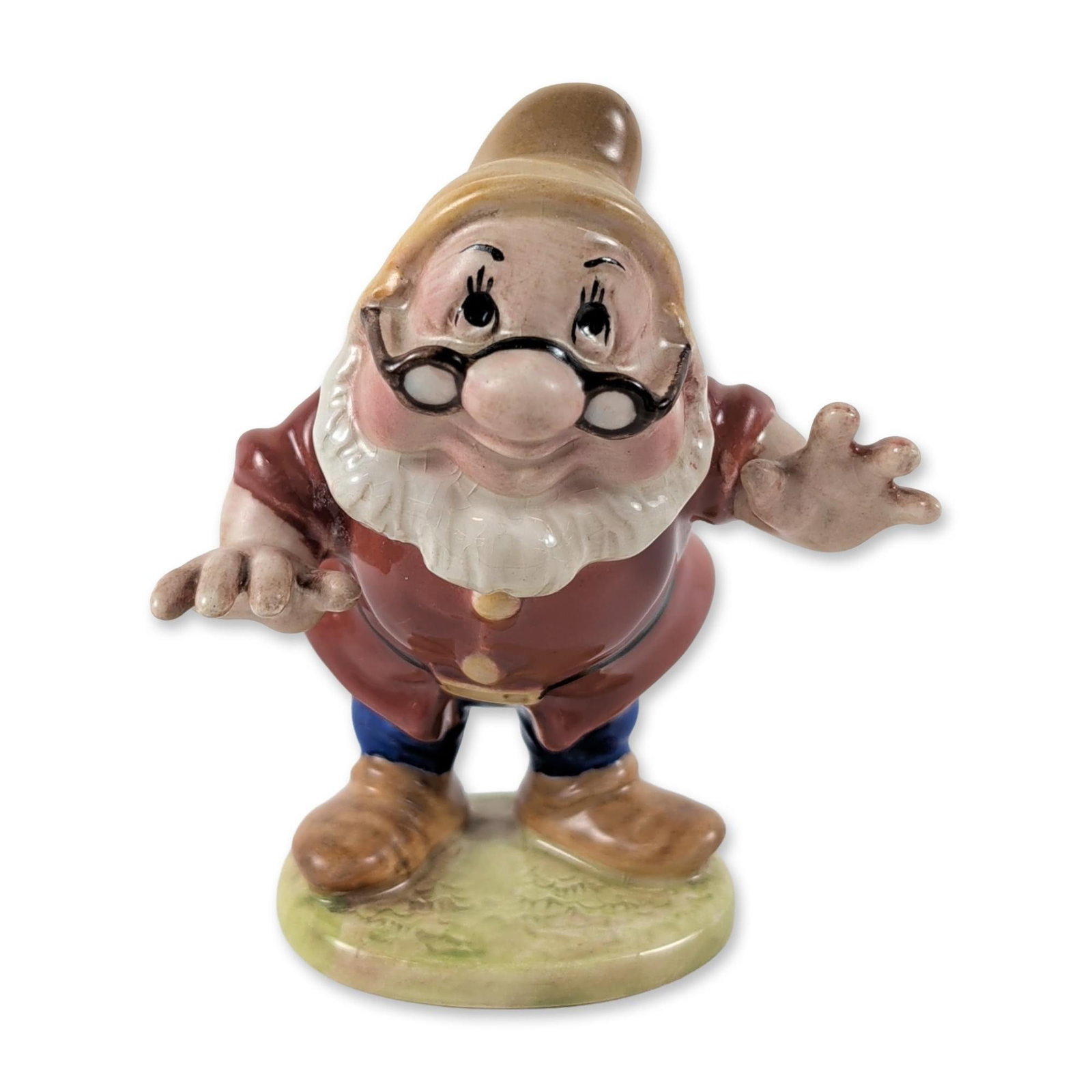 Beswick England Disney Doc Ceramic Figurine: Beswick Disney Doc ceramic figurine in glazed earthenware, depicting the character from Snow White and the Seven Dwarfs in a red tunic, blue trousers, and yellow-brown hat on a green mound base. Base 