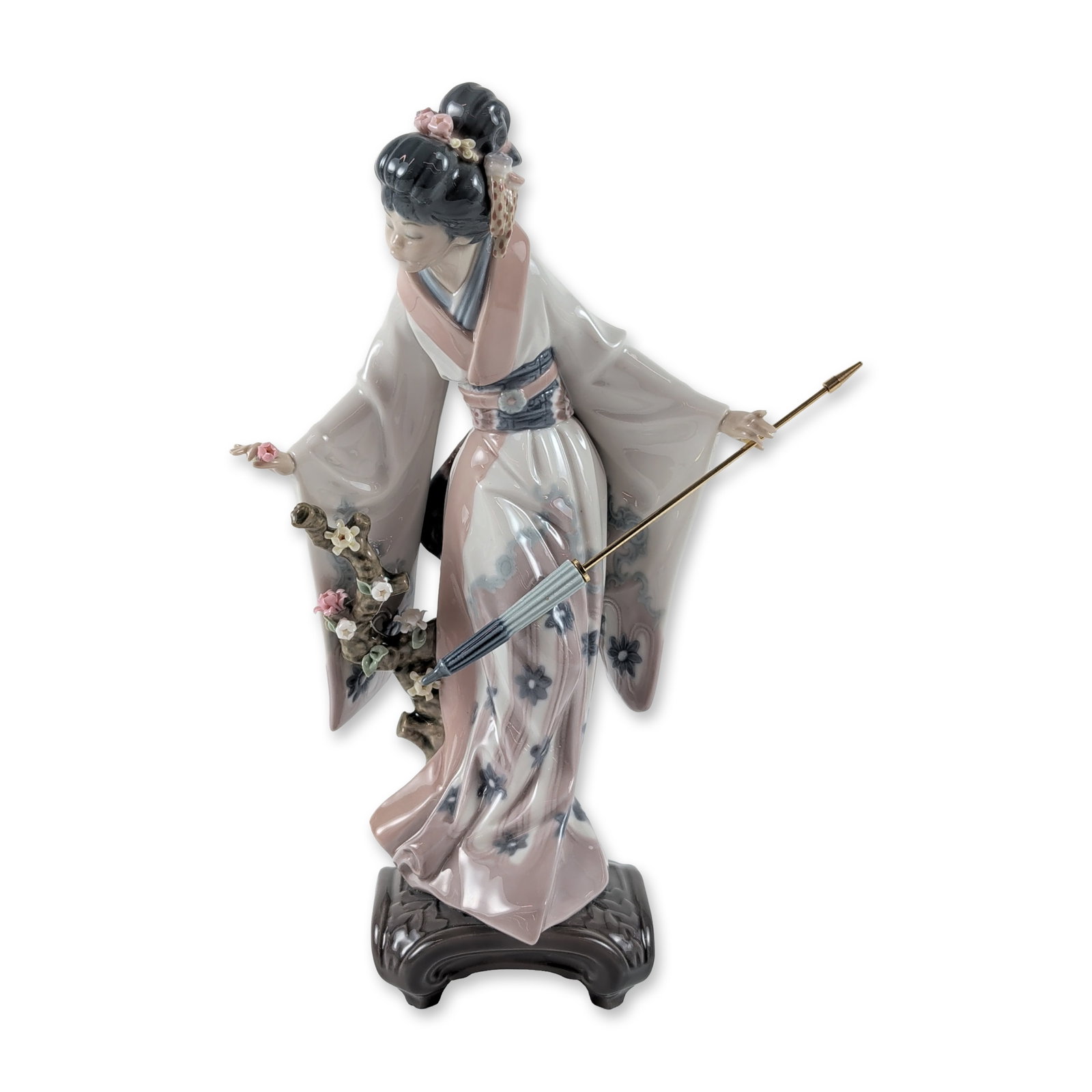 Lladro Porcelain Figurine, Teruko 1001451: The figure depicts a Japanese woman in traditional attire, featuring a light gray kimono with floral motifs and a dark blue obi with a floral pattern. The figure is posed next to a blossoming branch, 