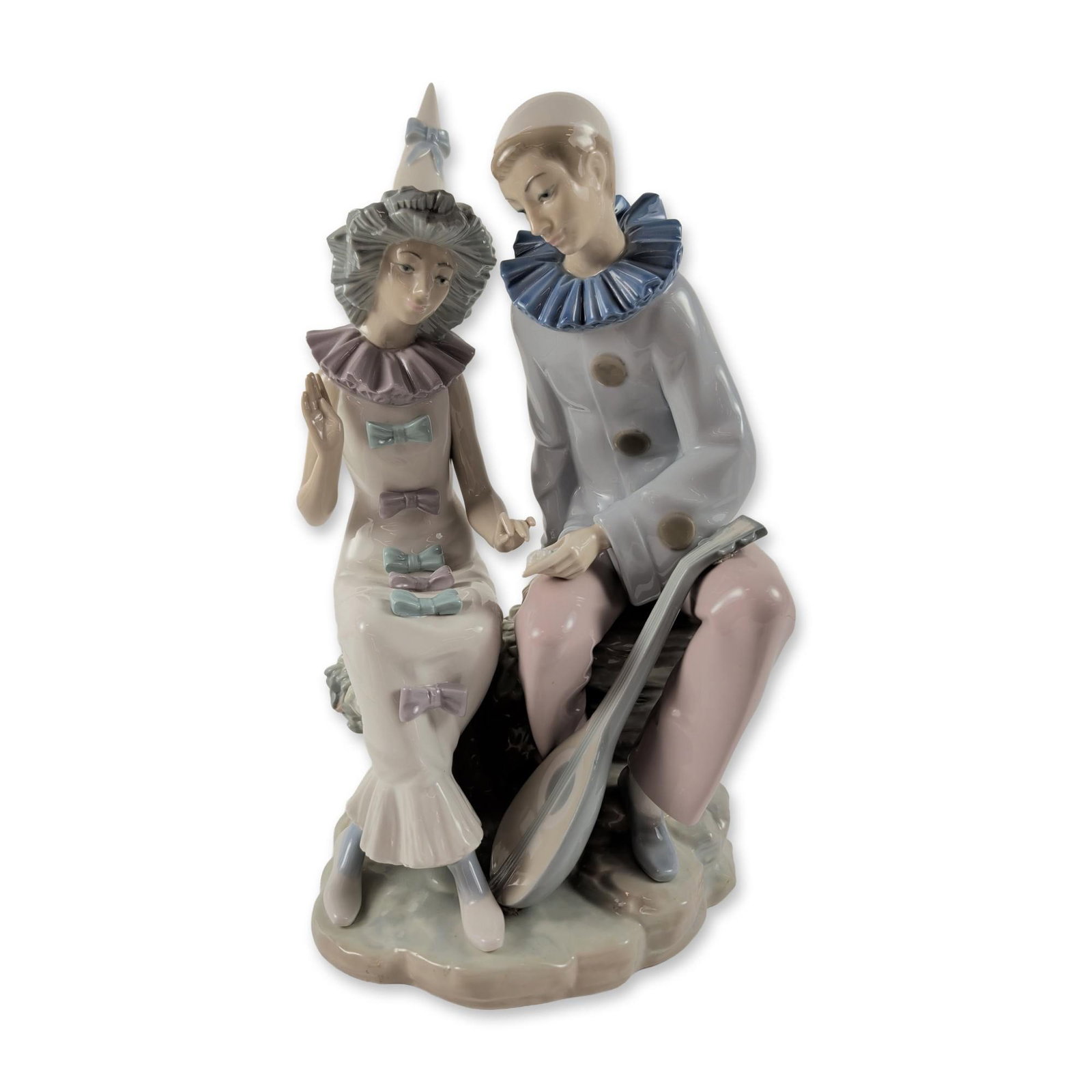 NAO by Lladro Spanish Porcelain Pierrot and Columbine Couple Sculpture: NAO Spanish glazed porcelain figurine depicting a seated Pierrot with a mandolin at his feet, alongside a seated Columbine in a coordinating circus costume. Both figures are decorated in soft pastel t