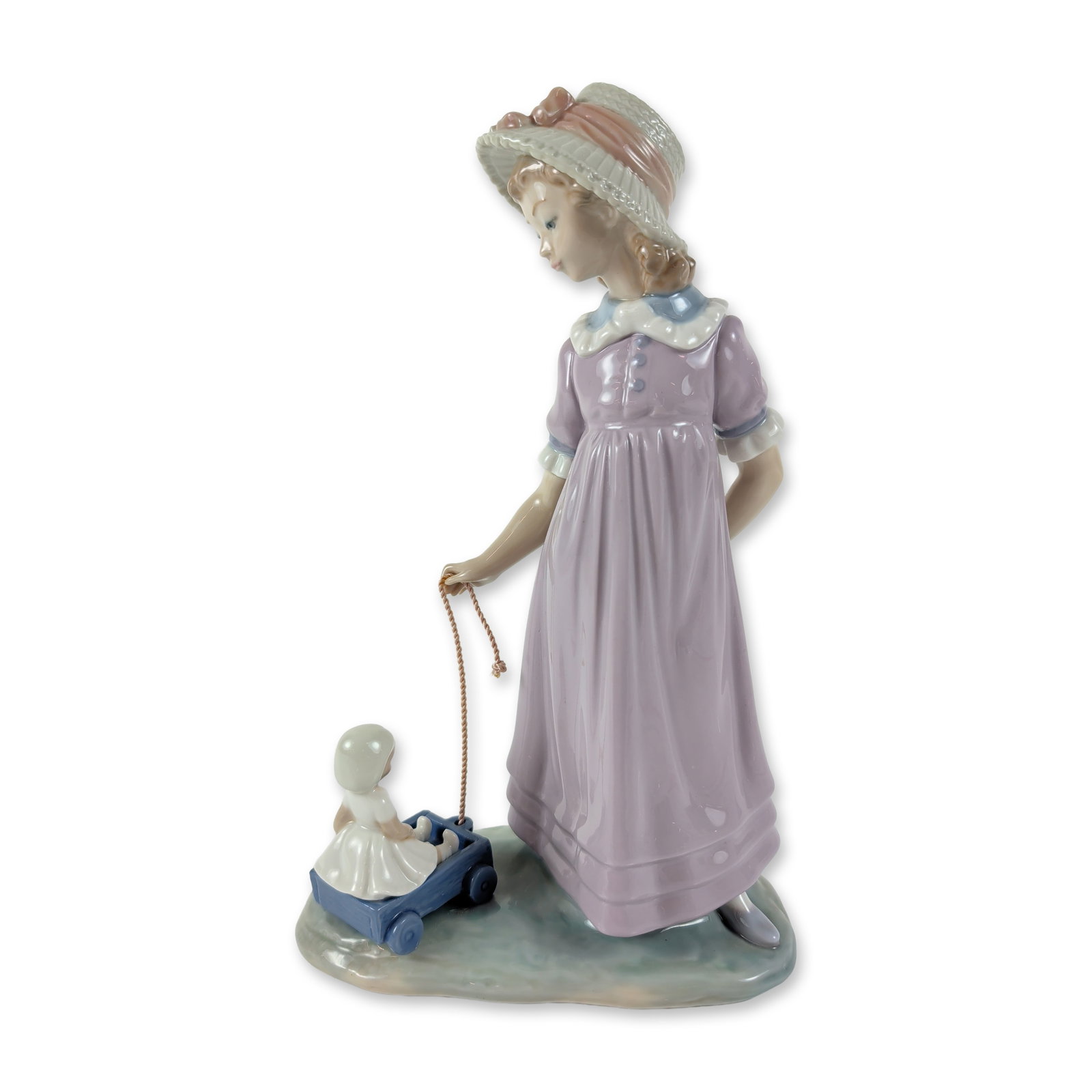 Lladro Porcelain Figurine, Girl with Toy Wagon 1005044: The figure depicts a young girl wearing a lavender dress and a wide-brimmed hat with a pink ribbon, pulling a blue toy wagon carrying a small doll. The underside bears the Lladro factory mark. Dimensi