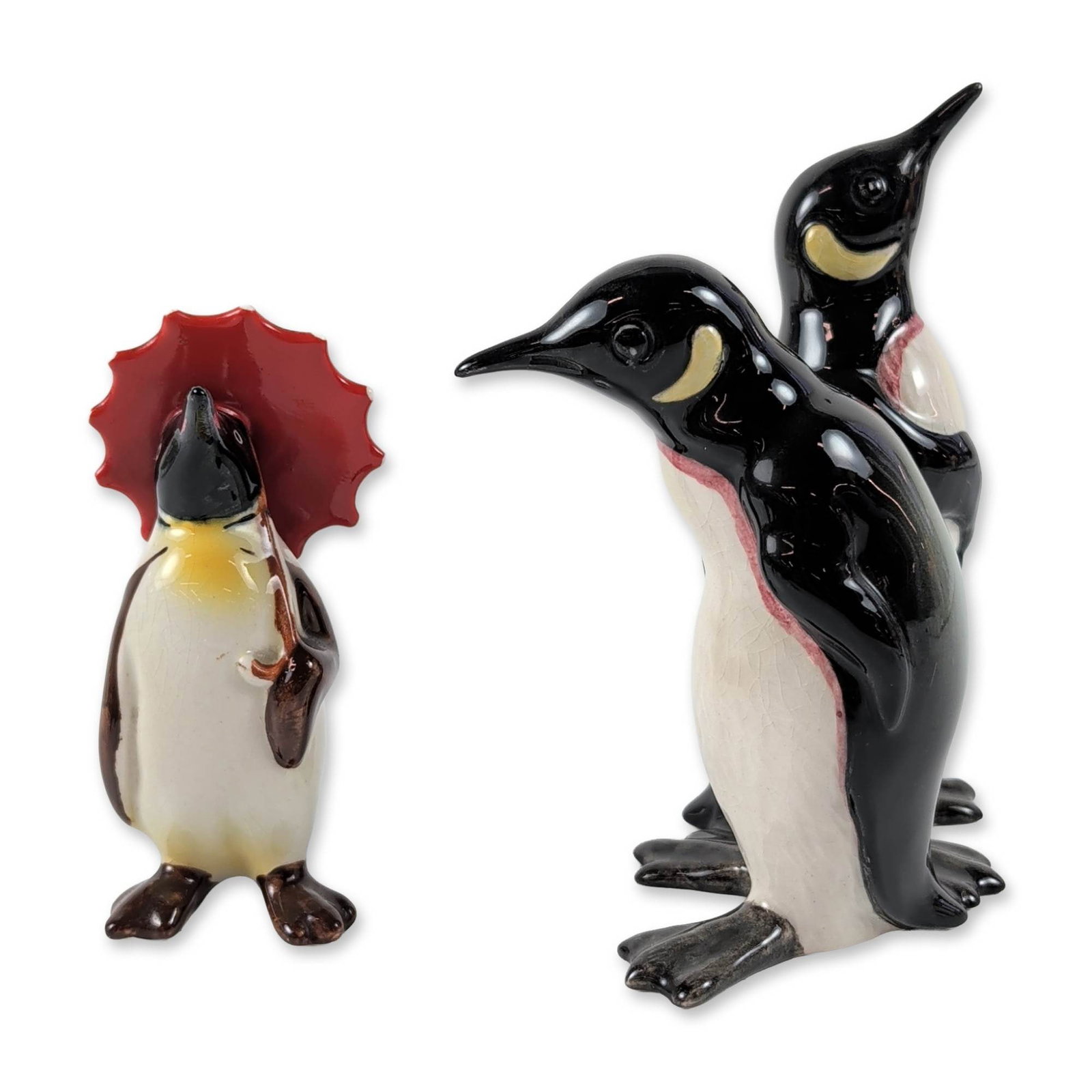 2pc Beswick England Glazed Ceramic Penguin Figurines: Beswick, England. Two ceramic penguin figurines in high-gloss glaze, including one model of a standing adult pair and one penguin chick with a red umbrella. The adult pair features an impressed model 