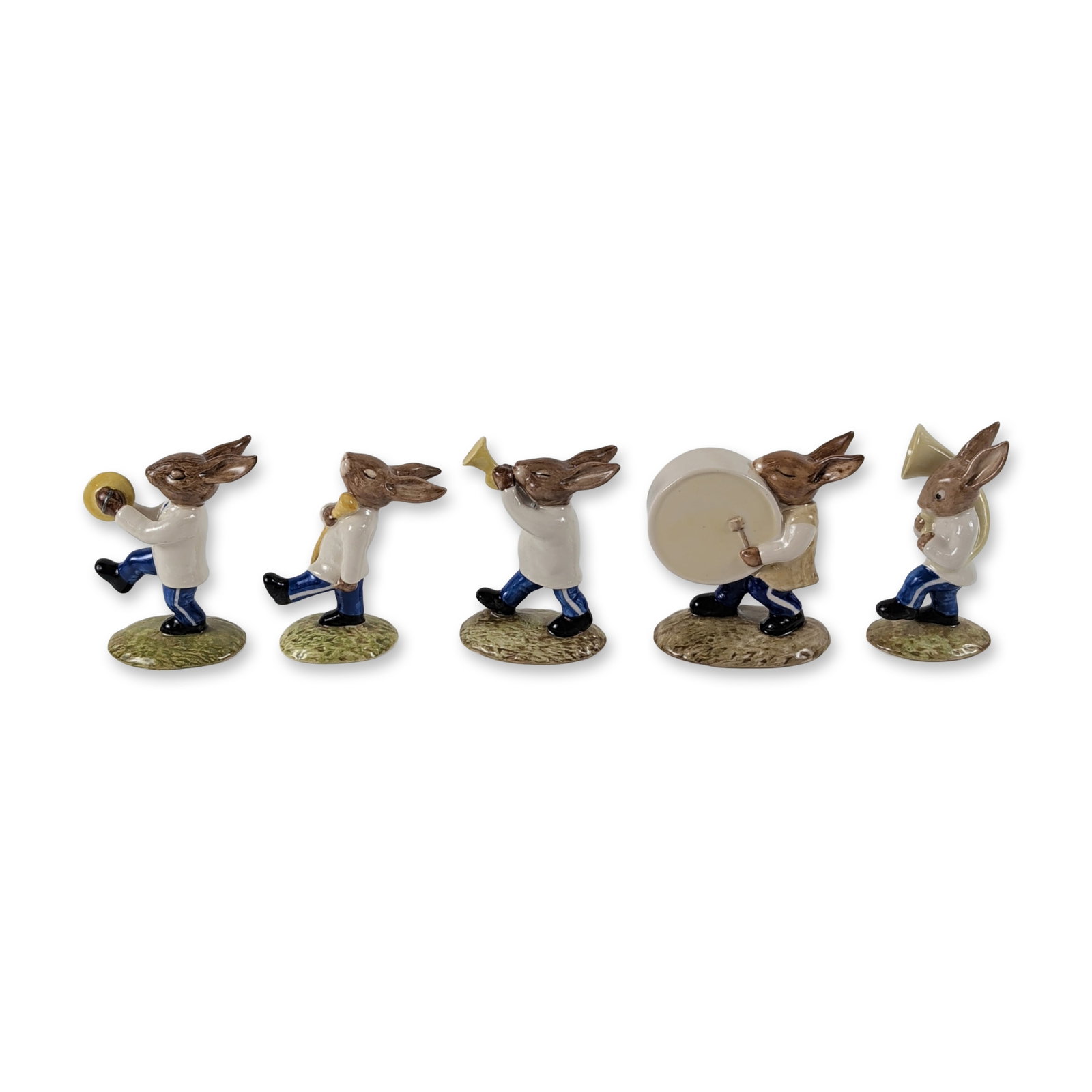 Set of Five Rare Colorway Royal Doulton Bunnykins Oompah Band Figurines: Royal Doulton, United Kingdom. Set of five glazed porcelain figurines from the Bunnykins Oompah Band series, featuring anthropomorphic rabbits dressed in white tunics and blue trousers. The collection