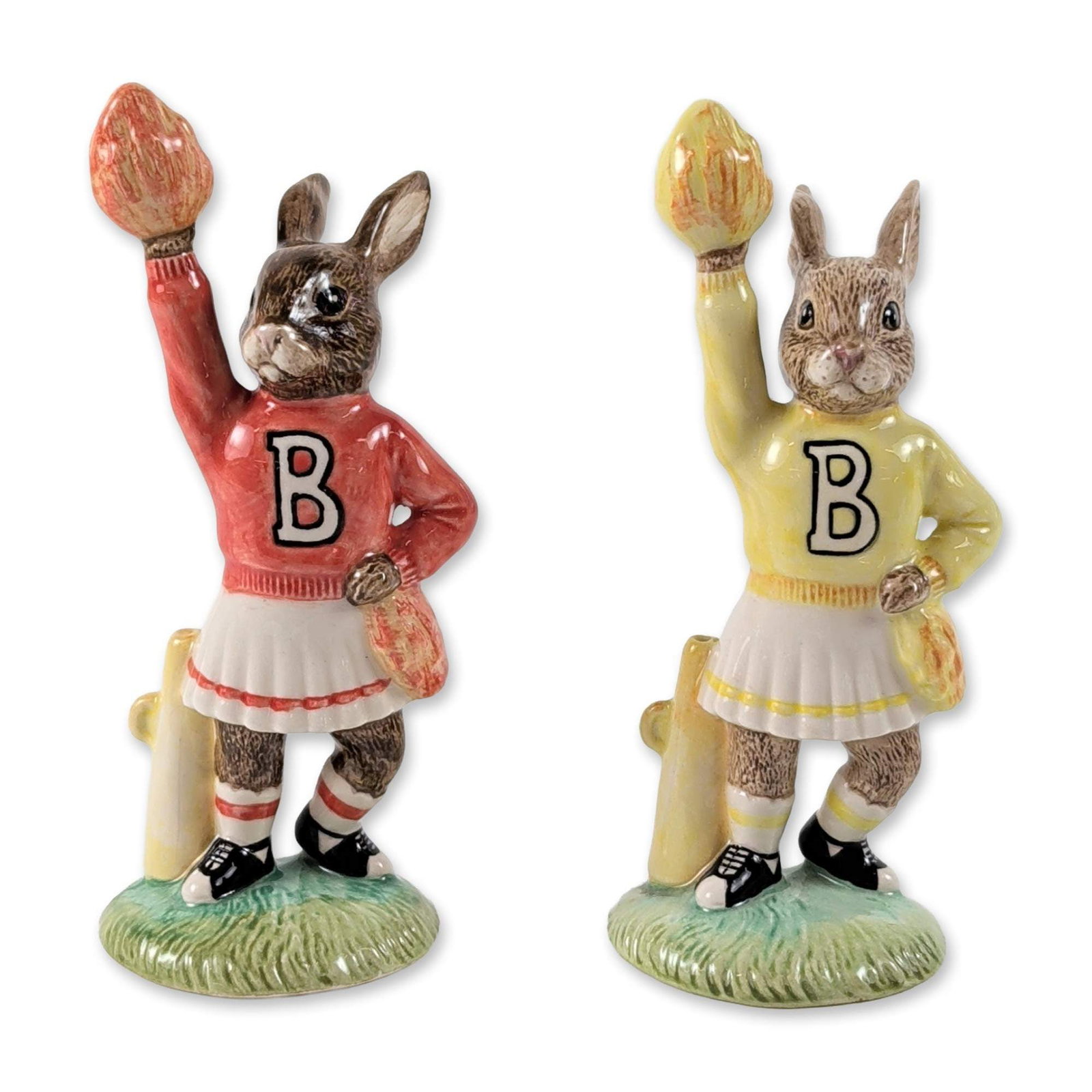 2pc Royal Doulton Cheerleader Bunnykins Figurines: Royal Doulton. Pair of Cheerleader Bunnykins ceramic figurines, including variants in red (DB 142) and yellow (DB 143). Each anthropomorphic rabbit is depicted in a cheerleading sweater with a black l