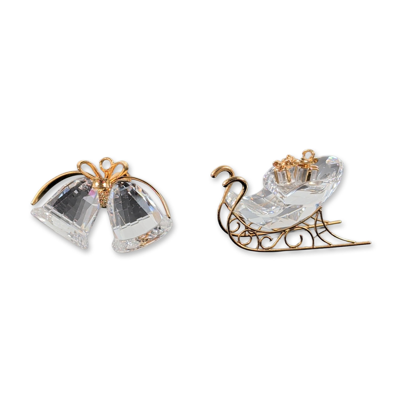 2pc Swarovski Crystal and Gold-Tone Figurines: Swarovski. Two figurines in faceted clear lead crystal with gold-tone metal accents. The first is a miniature sleigh featuring a crystal body and decorative metal runners with scrollwork detailing. Th