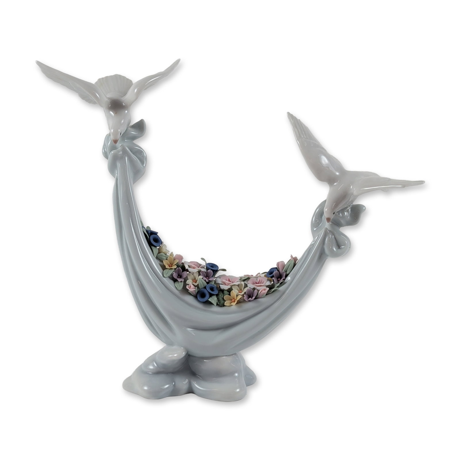 Lladro Glossy Porcelain Figurine, Petals of Peace 1006579: Featuring two white doves perched on a floral-garland draped crescent base. The piece displays a contrast between the high-gloss glaze of the birds and base and the matte bisque finish of the hand-app