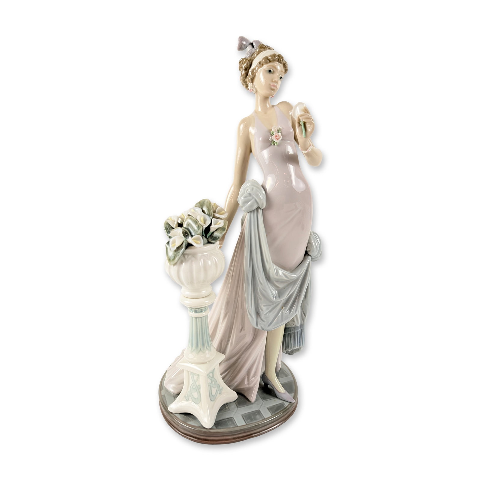 Lladro Porcelain Figurine, A Touch of Class 1005377: Features an elegant woman in a lavender floor-length gown with a blue wrap, standing beside a fluted pedestal and vase filled with white calla lilies. The circular base is decorated with a grey and bl