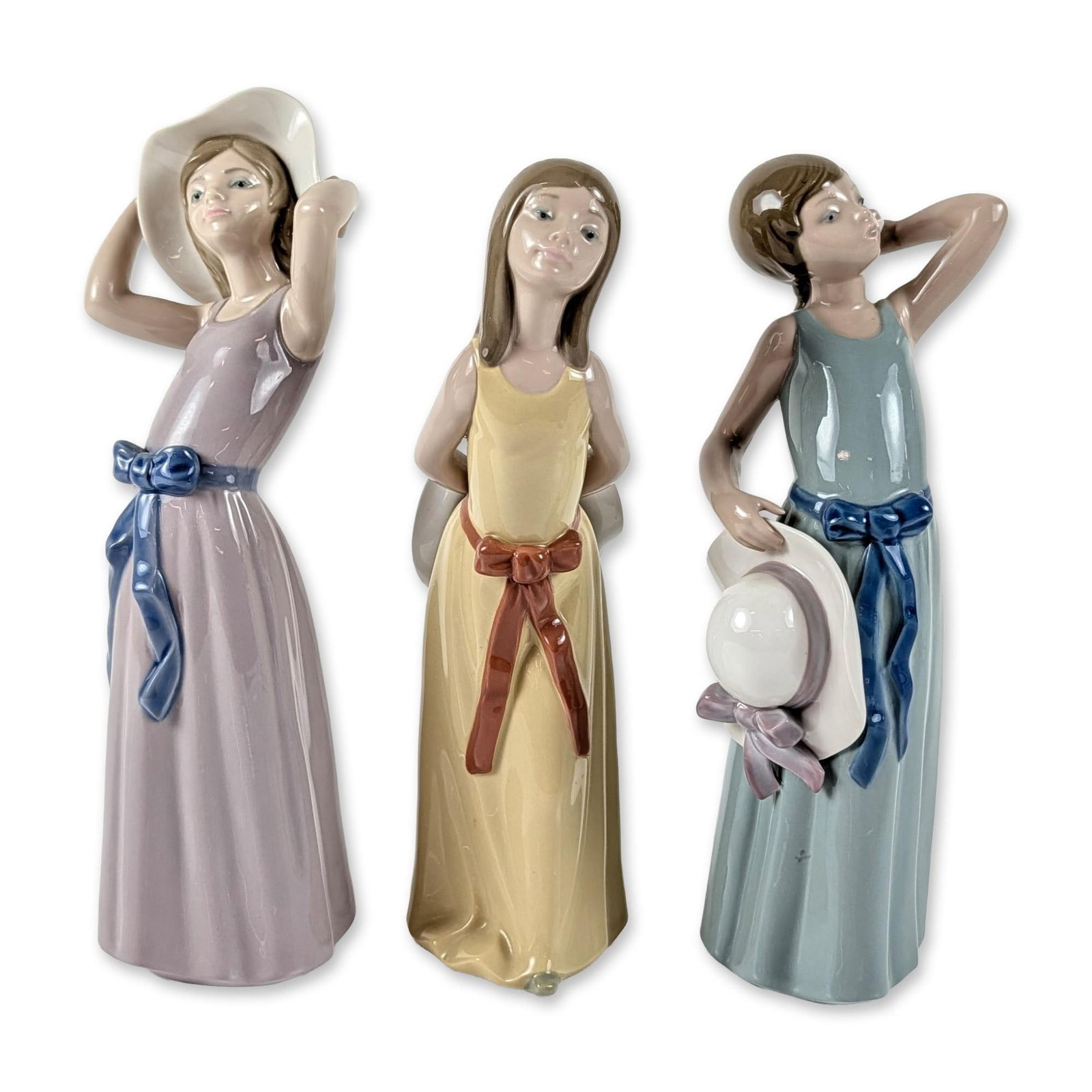 3pc Lladro Porcelain Figurines, Coy, Naughty, and Prissy: Collection of three Lladro porcelain figurines depicting young girls in long, high-waisted summer dresses with contrasting sash bows and wide-brimmed sun hats. The group includes Coy (1005011), depict