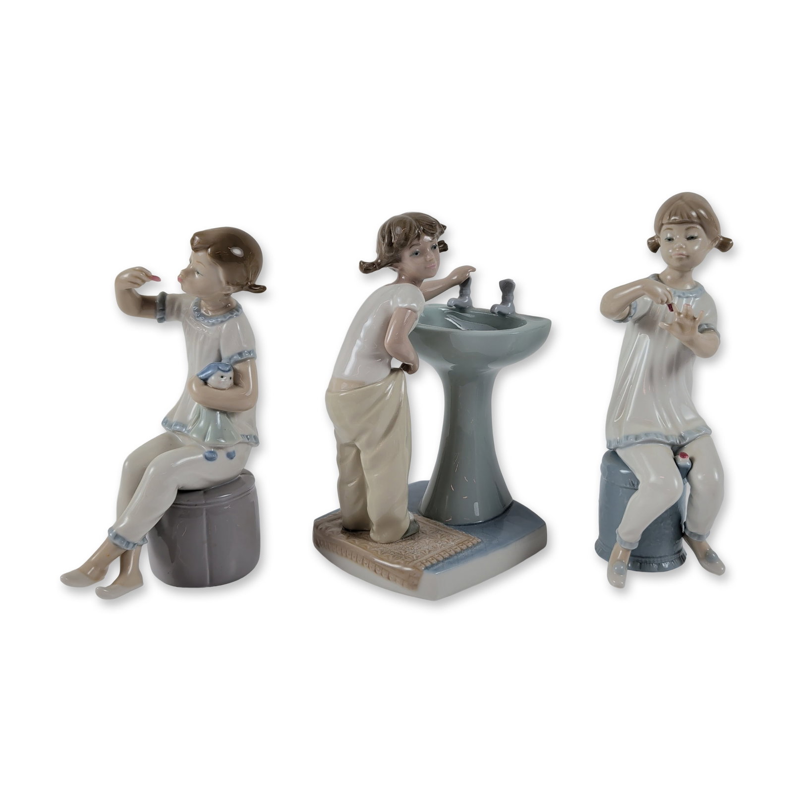 3pc Lladro Porcelain Figurines, Girl with Doll, Clean Up Time, and Girl Manicuring: Collection includes Girl with Doll which models a girl on a blue stool applying lipstick while holding her doll (1001083), Clean Up Time (1004838) depicting a girl at a washbasin, and Girl Manicuring 