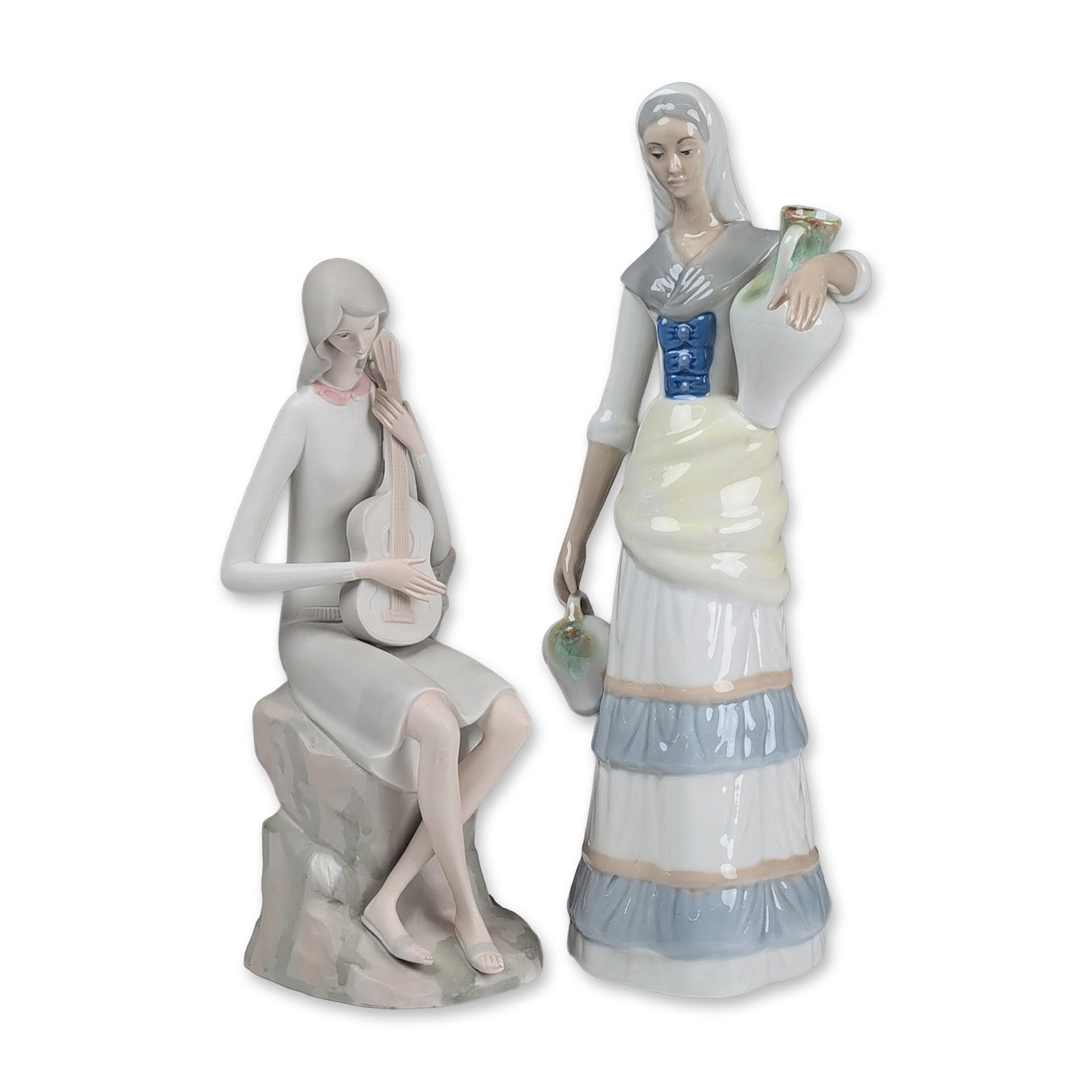 2pc Spanish Glazed and Bisque Porcelain Figurines including Tengra: Spanish, mid-to-late 20th century. The first figurine, marked by Tengra, depicts a standing woman in peasant dress carrying two water pitchers. This figure features a blue laced bodice and a tiered sk