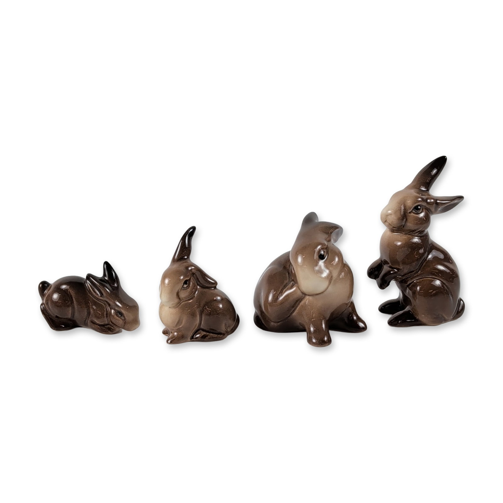 Group of Four Beswick Ceramic Rabbit Figurines: English ceramic figurines by Beswick, in high-gloss glazed ceramic featuring a naturalistic mottled brown and tan hare's fur glaze. The collection consists of four figures in various poses, including 