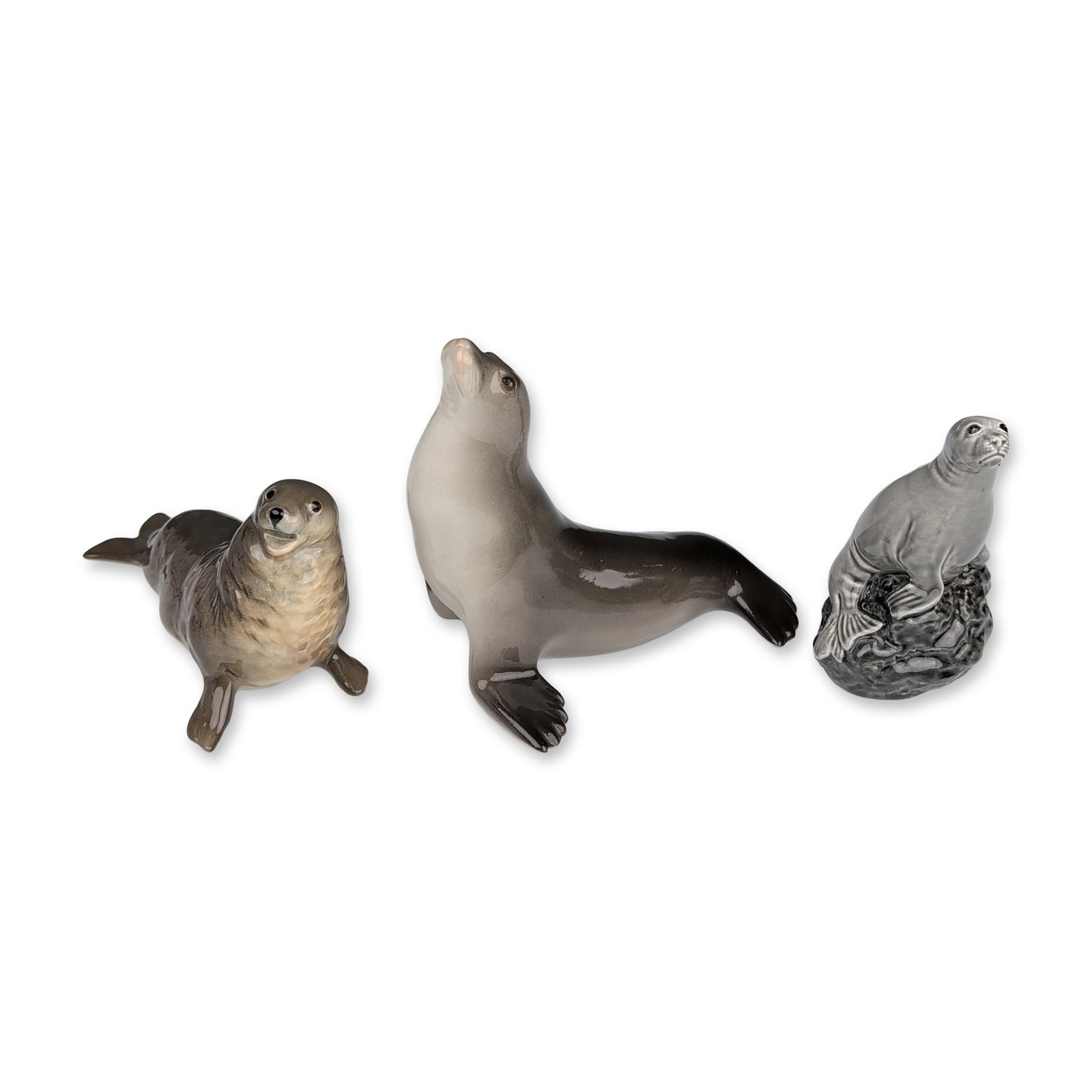 3pc Beswick and Lomonosov Porcelain Seal Figurines: Trio of vintage glazed ceramic and porcelain seal figurines. Includes a Beswick for Beneagles Scotch Whisky miniature decanter modeled as a seal on a rock, with a black printed mark to the underside i