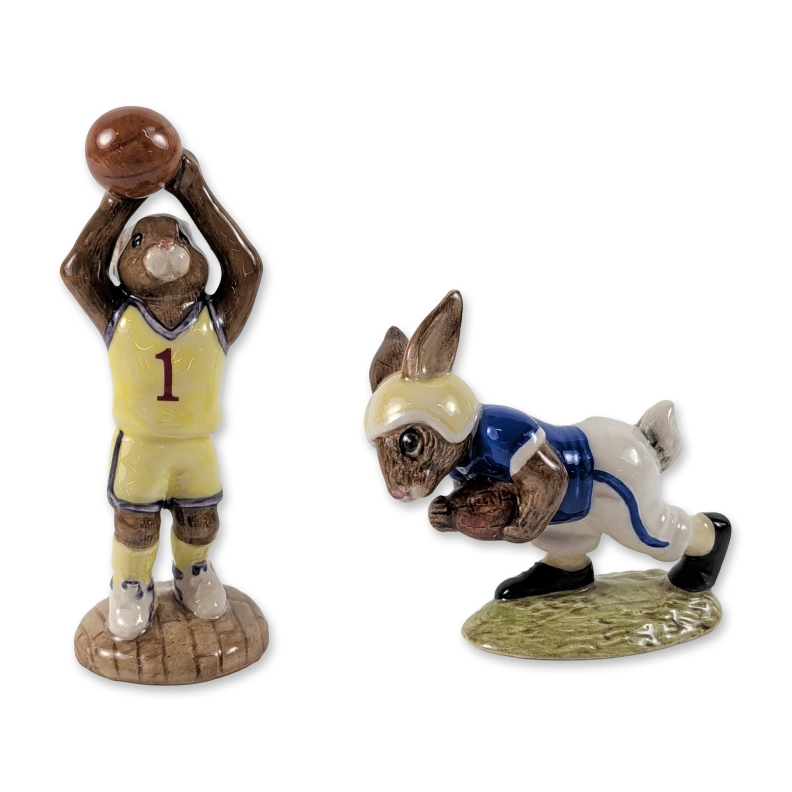 2pc Royal Doulton Bunnykins Figurines: Royal Doulton. Pair of ceramic figurines from the Bunnykins collection with sports themes. The Basketball Bunnykins figurine (DB 262) depicts a rabbit in a yellow uniform on a wooden court base, marke