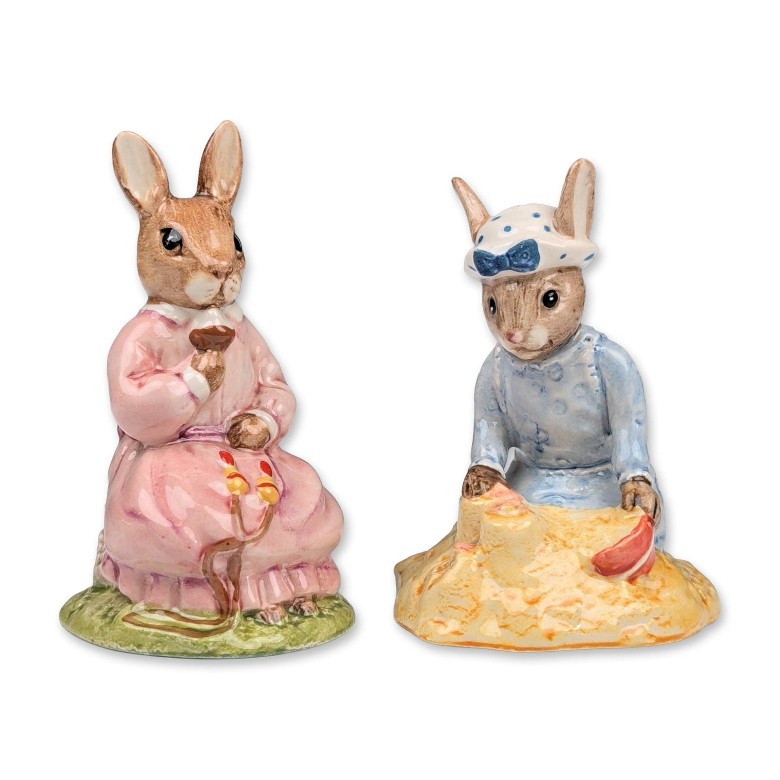 2pc Royal Doulton Bunnykins Porcelain Figurines: Royal Doulton. Pair of Bunnykins figurines in glazed porcelain, featuring Seaside Bunnykins and Polly Bunnykins characters. Seaside Bunnykins (DB 177) depicts a rabbit in a blue dress and bonnet seate