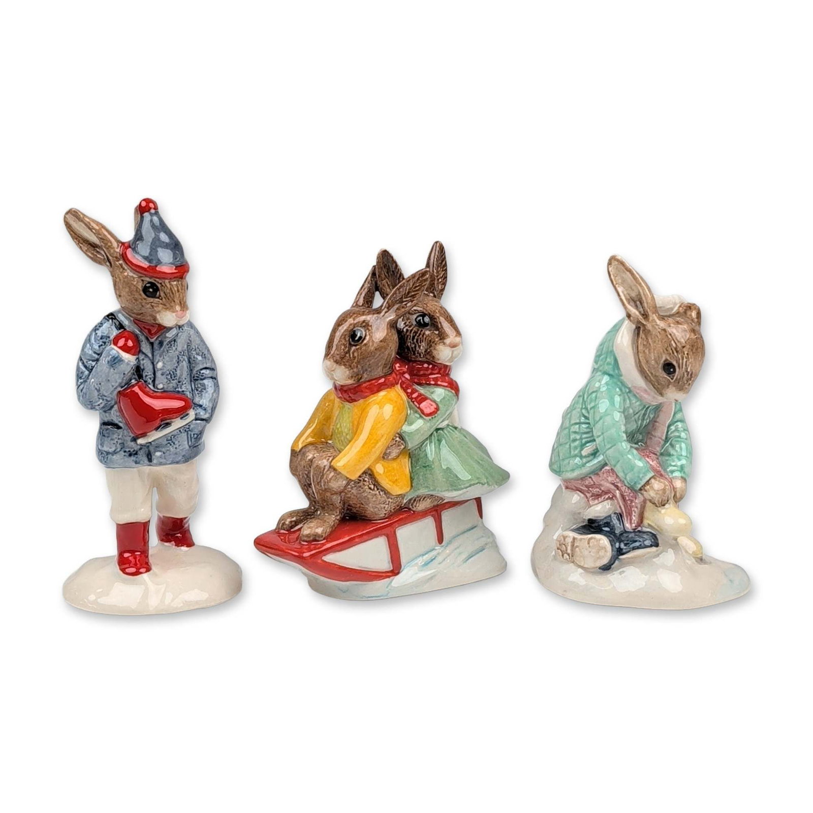 3pc Royal Doulton Bunnykins Ceramic Figurine: Trio of Royal Doulton Bunnykins glazed porcelain figurines with winter themes. The collection includes Girl Skater (DB 153), featuring a rabbit in a green checkered coat and pink skirt; Billie & Bunti
